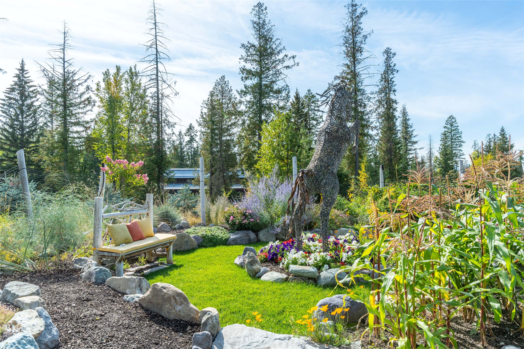 Garden lawn with flower beds, a cushioned wooden bench, and a tall metal animal sculpture.