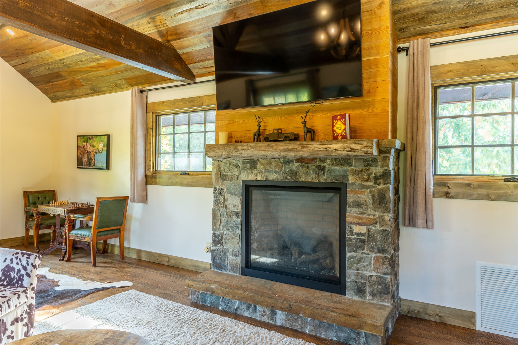 Living room with a stone fireplace, timber mantel, and vaulted wood ceiling.