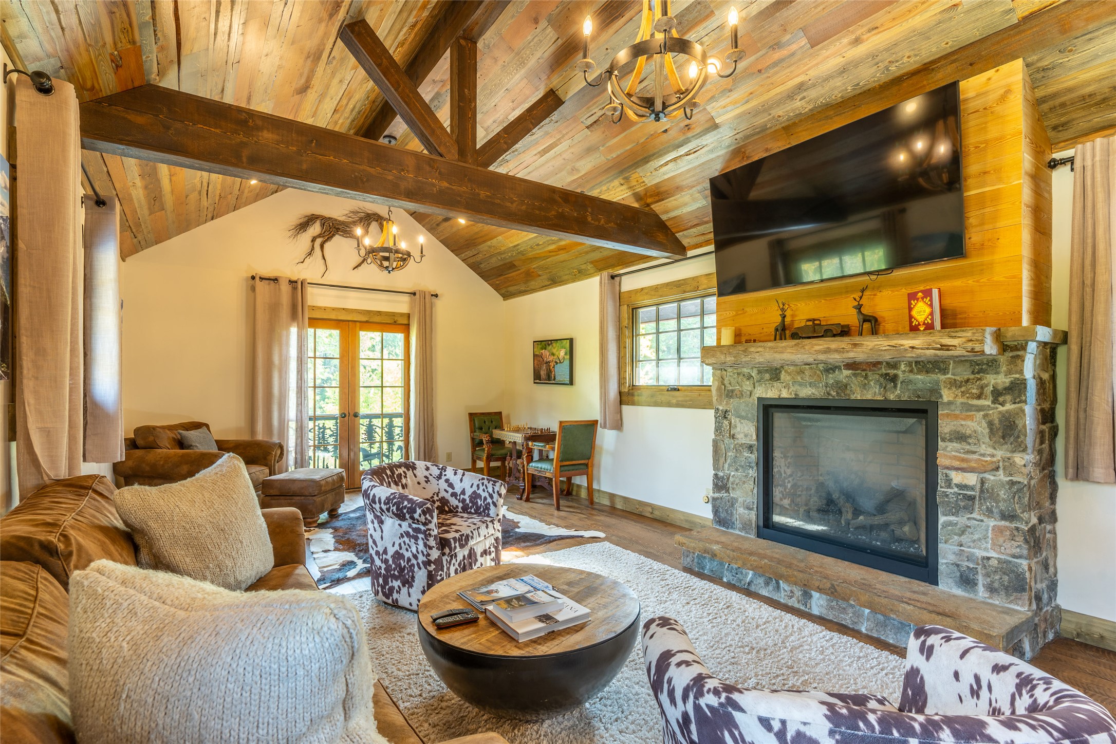 Living room with a vaulted wood ceiling, exposed beams, and a stone fireplace beneath a mounted television.