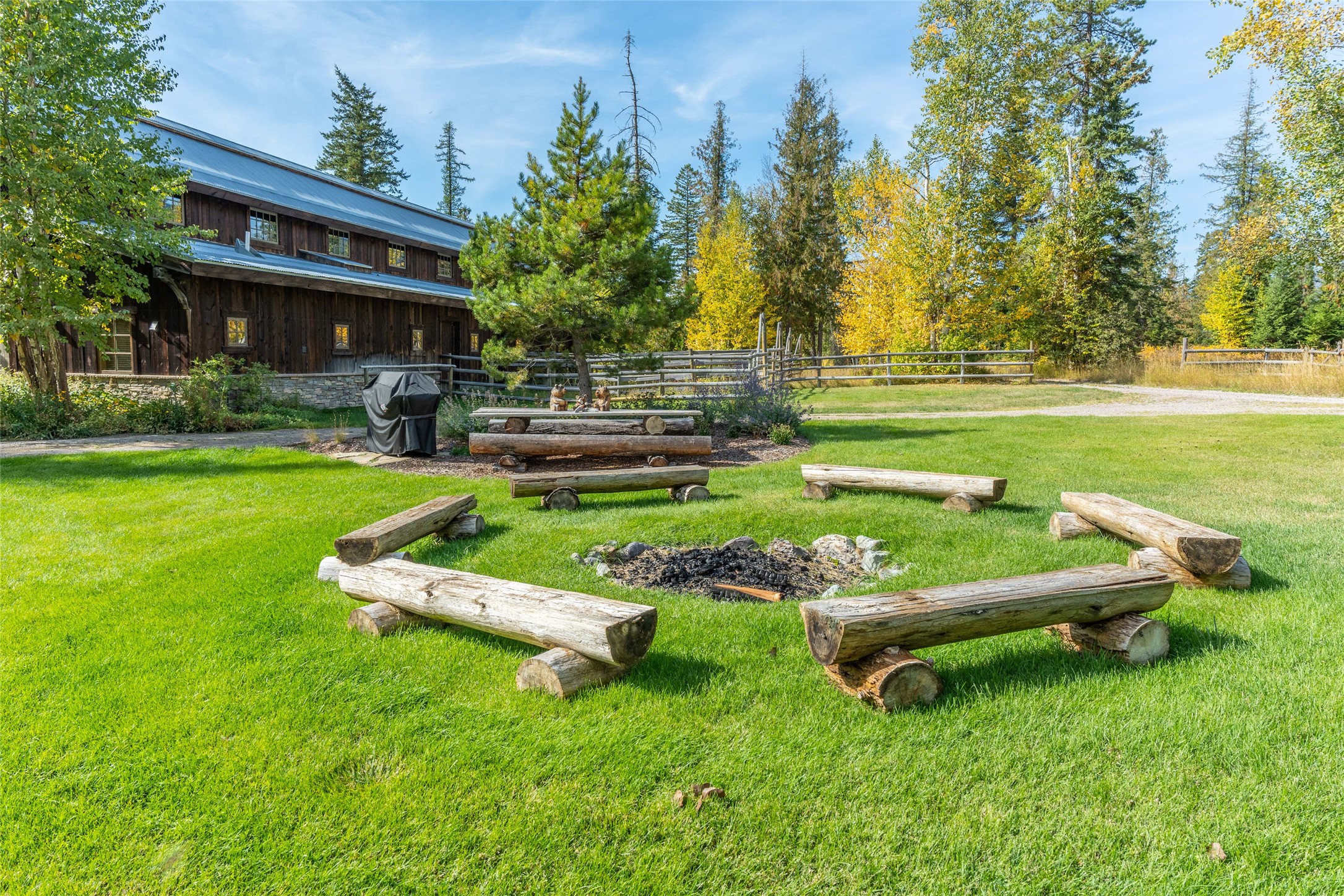 Rustic wood home beside a lawn with a circular log fire pit seating area.