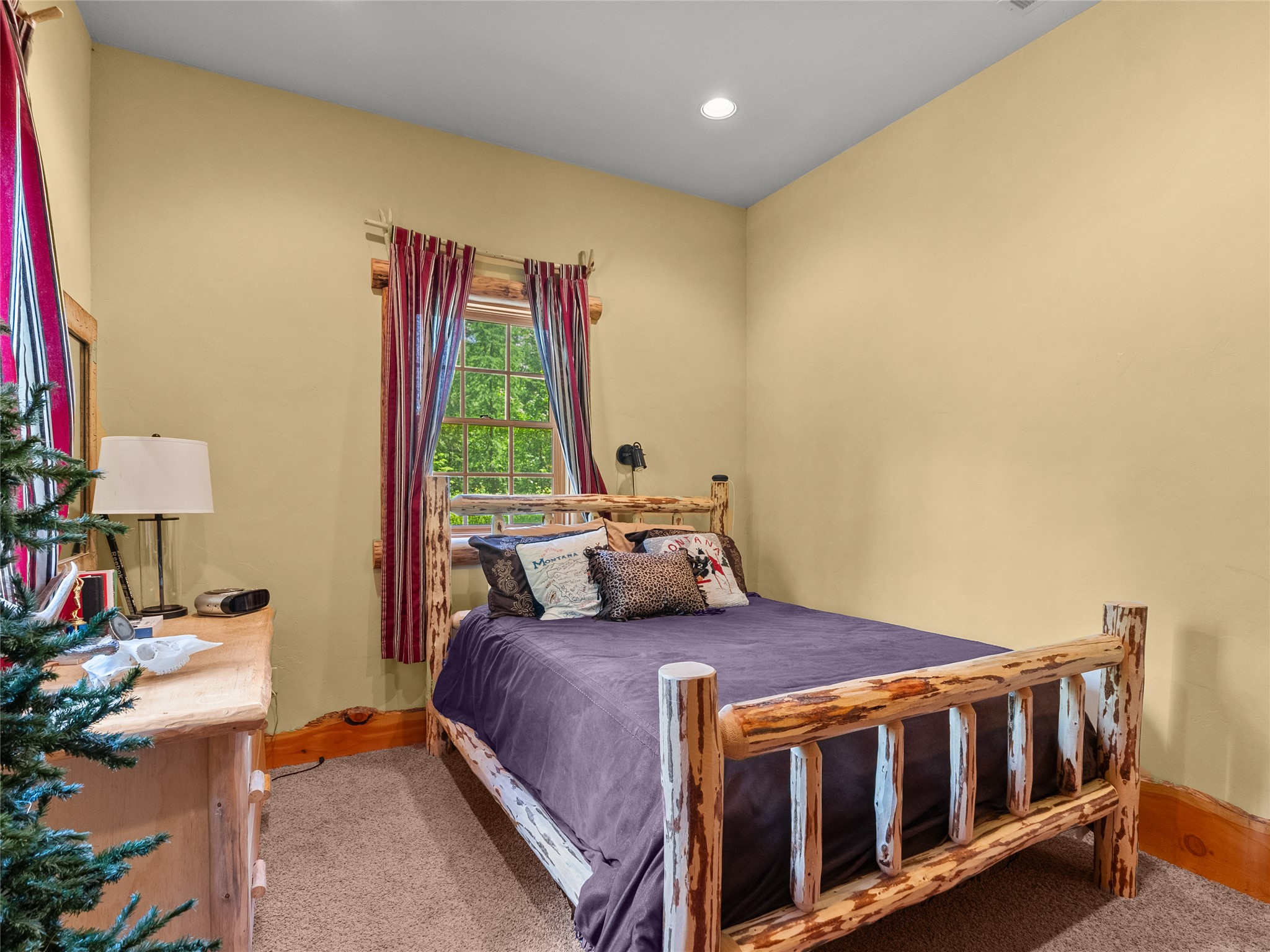 Bedroom with a rustic log bed, purple bedding, and a window framed by striped curtains.