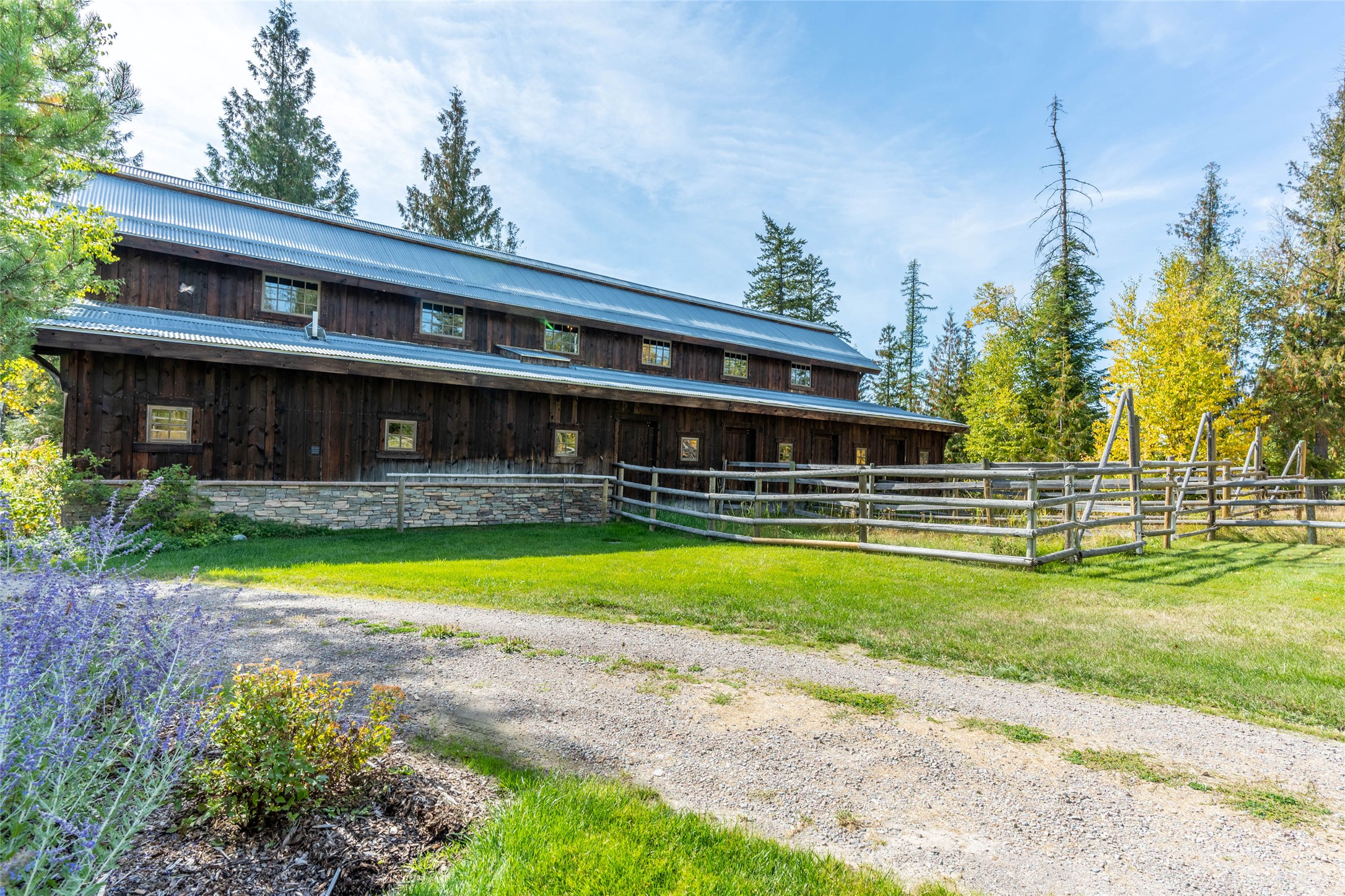 Dark timber home with a metal roof, stone foundation, and rustic fencing amid autumn trees.