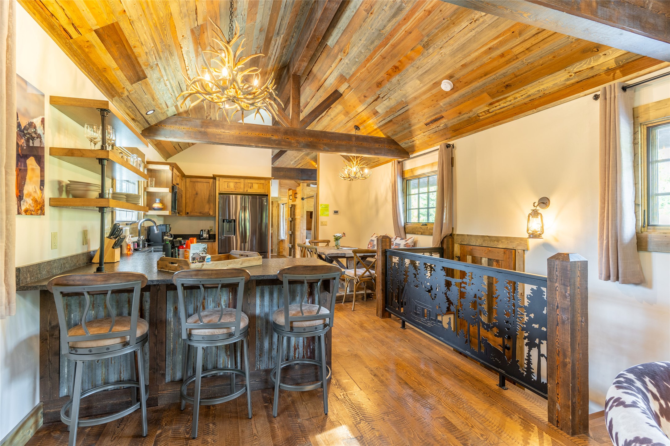 Rustic kitchen and dining area with a large island beneath a vaulted reclaimed-wood ceiling and antler chandeliers.