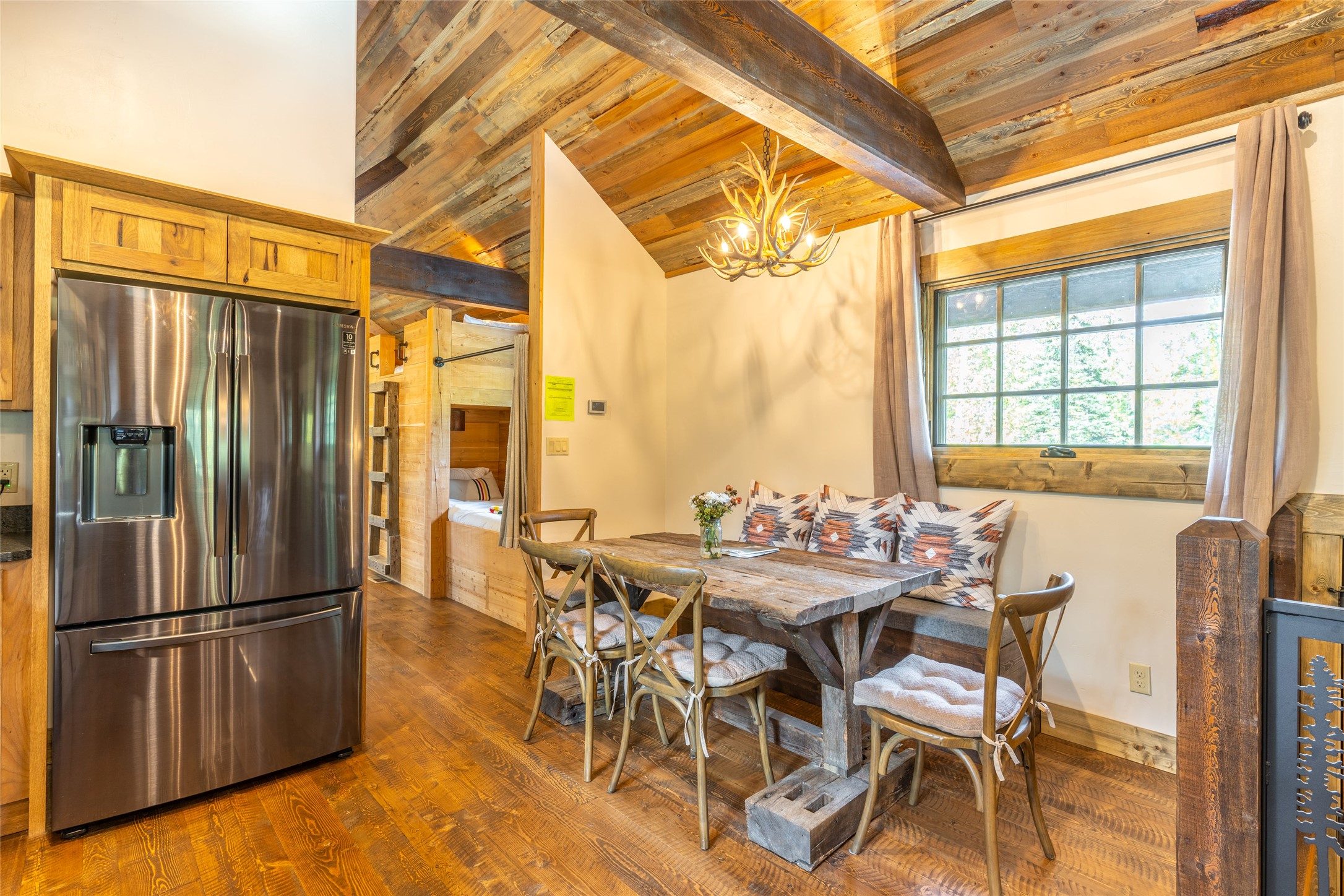 Rustic kitchen and dining nook with reclaimed-wood beams, a timber table, built-in bench, and antler chandelier.