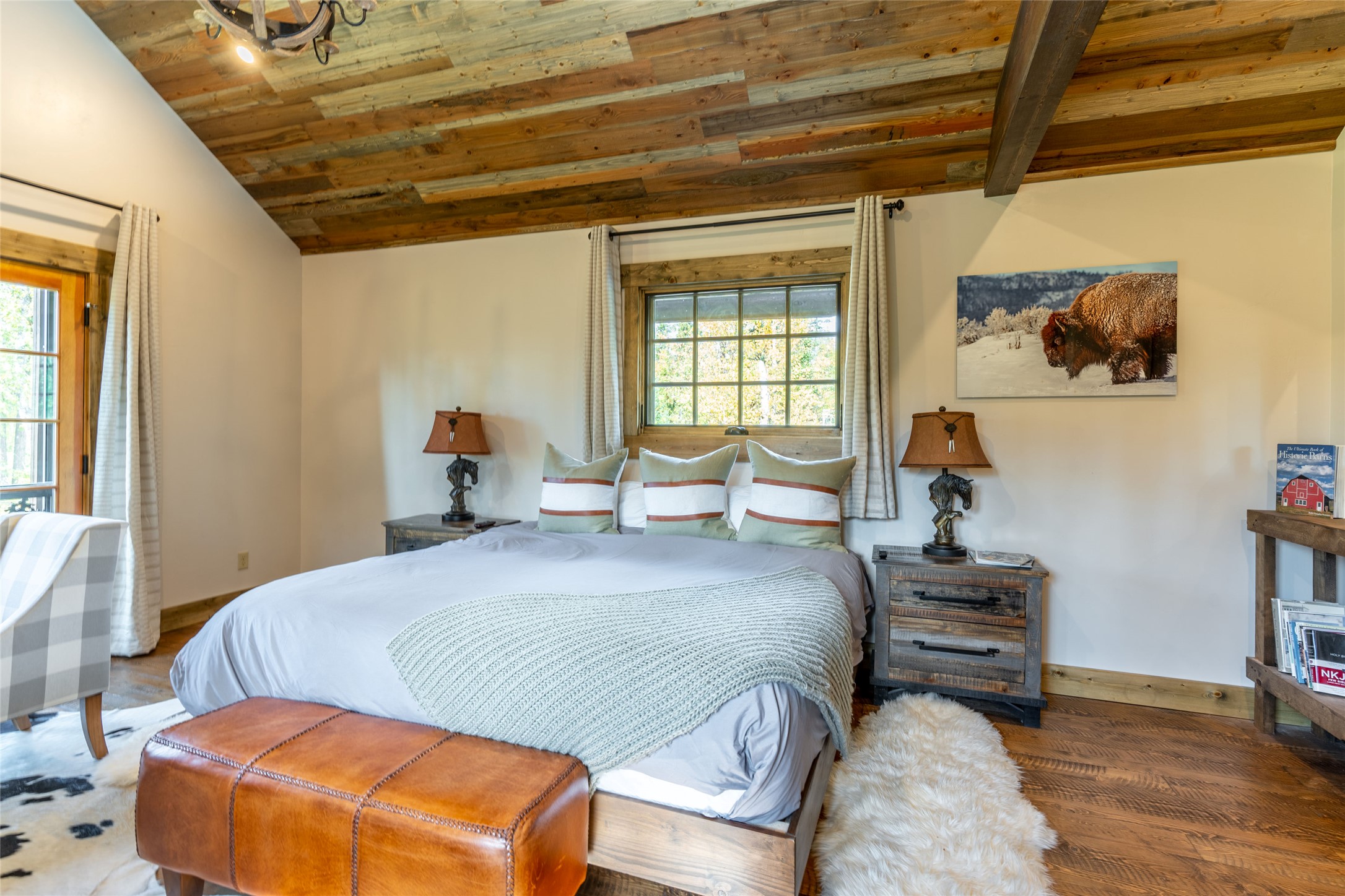 Rustic bedroom with a wood-plank ceiling, large bed, leather bench, and buffalo photograph.