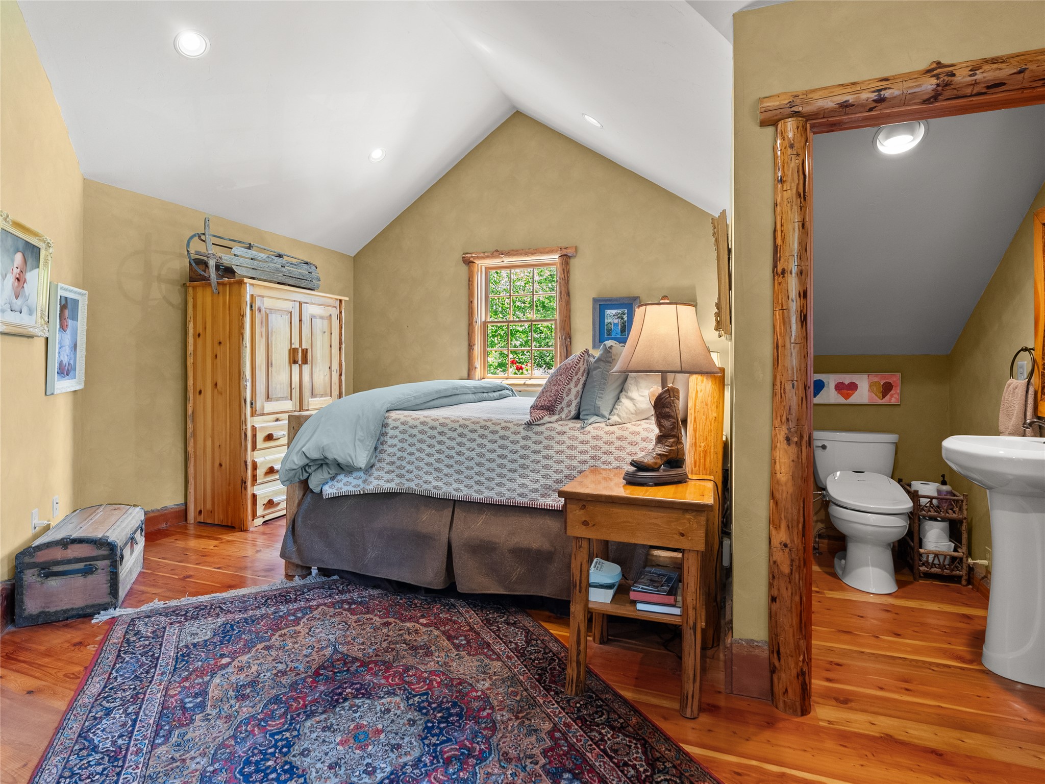 Bedroom with vaulted ceiling, rustic wood furnishings, patterned rug, and an adjoining bathroom.