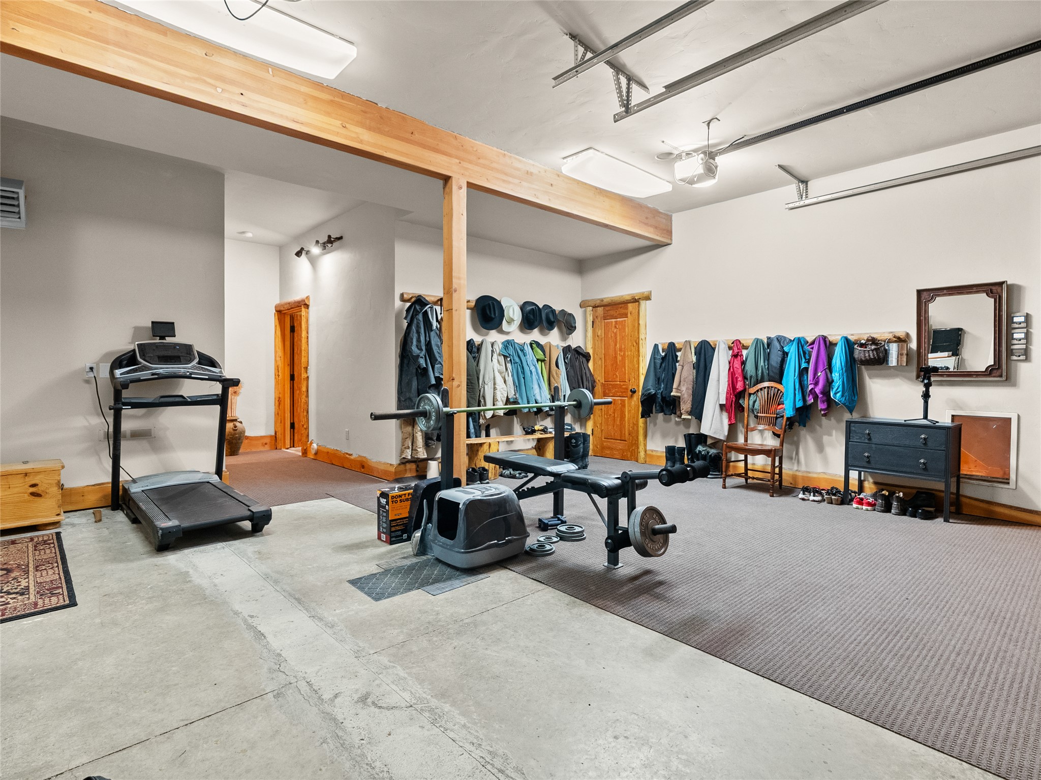 Garage gym with a treadmill and weight bench; coats and hats hang along the walls.