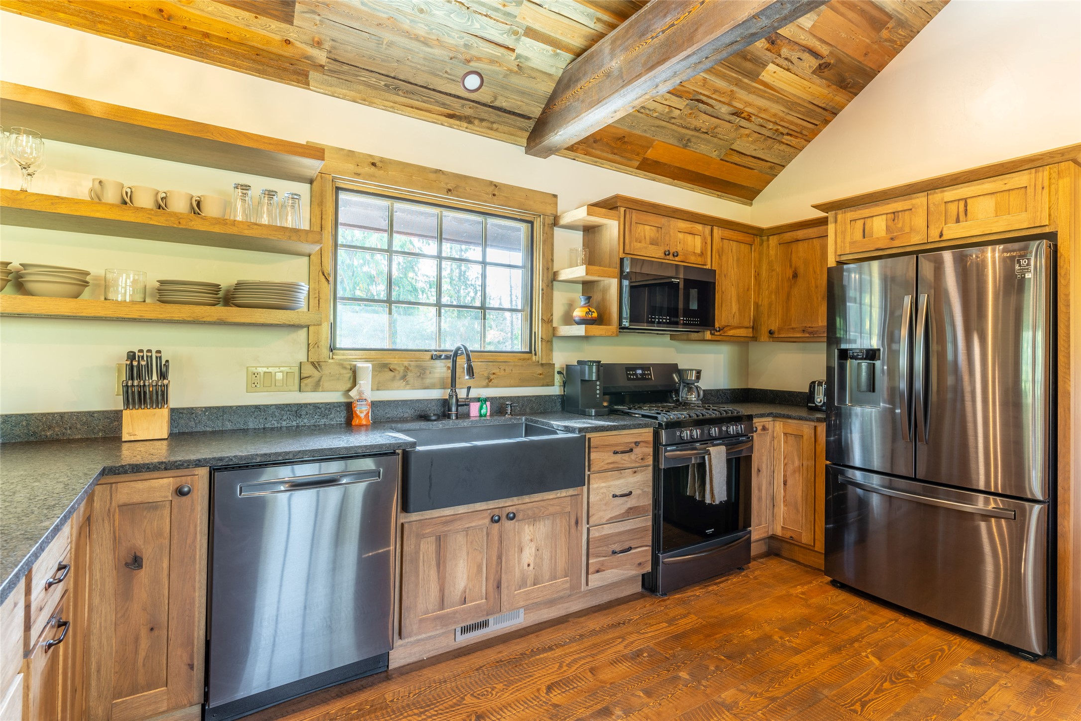 Rustic kitchen with wood cabinets, vaulted plank ceiling, farmhouse sink, and stainless steel appliances.