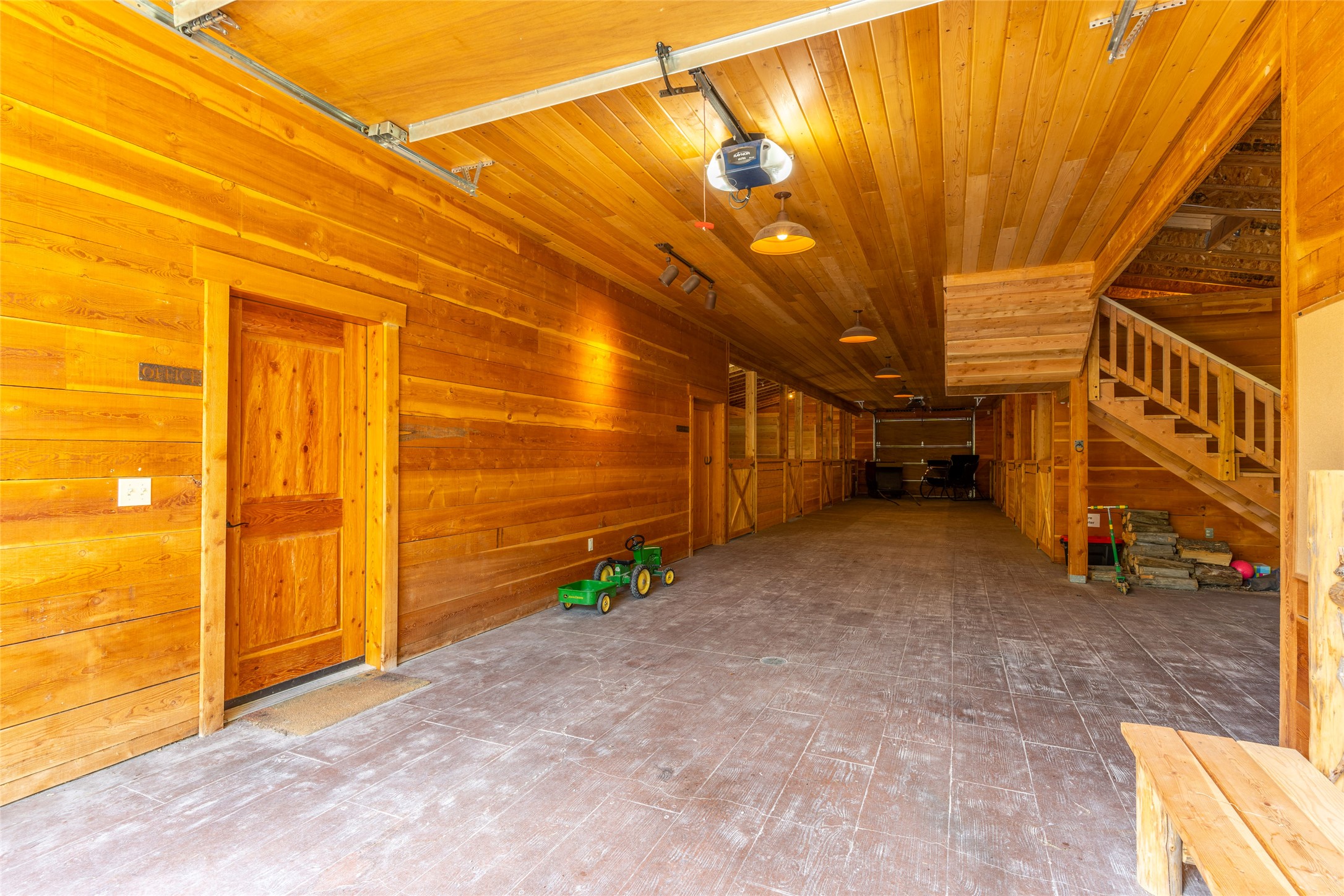 Spacious wood-paneled garage with an office door, staircase, and green toy tractor and wagon.