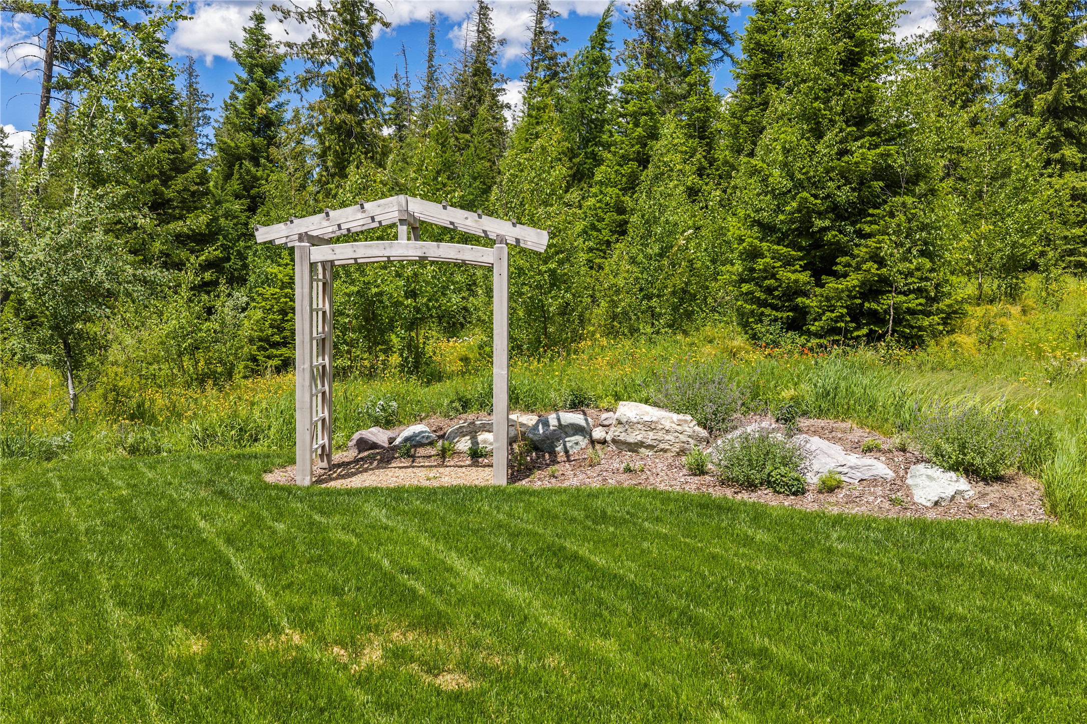 Lawn and wooden garden arbor beside a rock garden, with dense woodland behind.