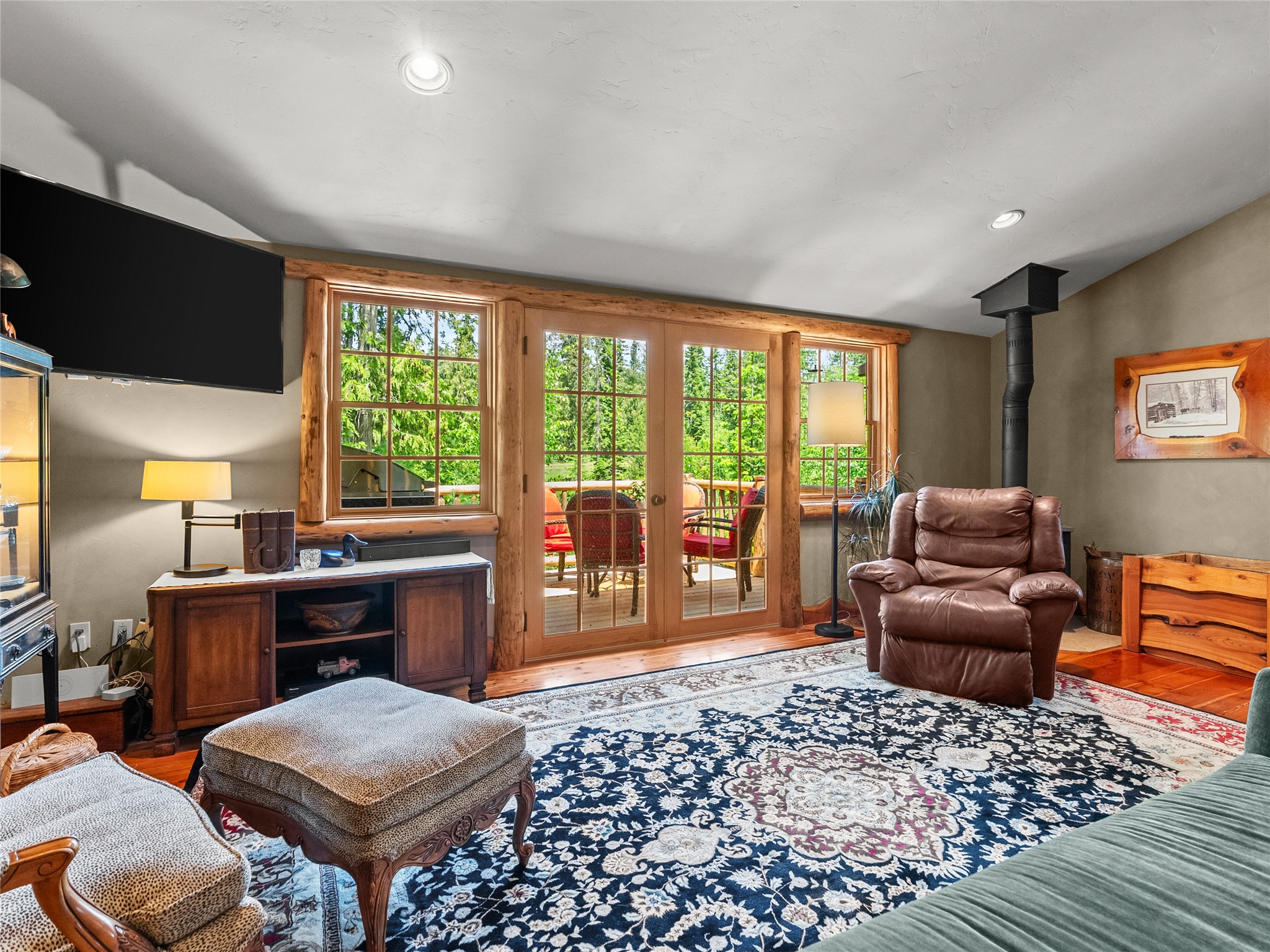 Living room with log-trimmed French doors opening to a deck, leather recliner, and large patterned rug.