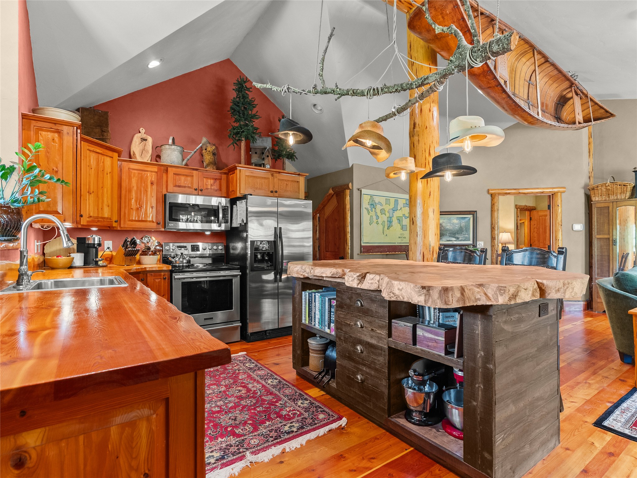 Rustic kitchen with a live-edge island, wood cabinetry, stainless appliances, and a canoe suspended from the ceiling.