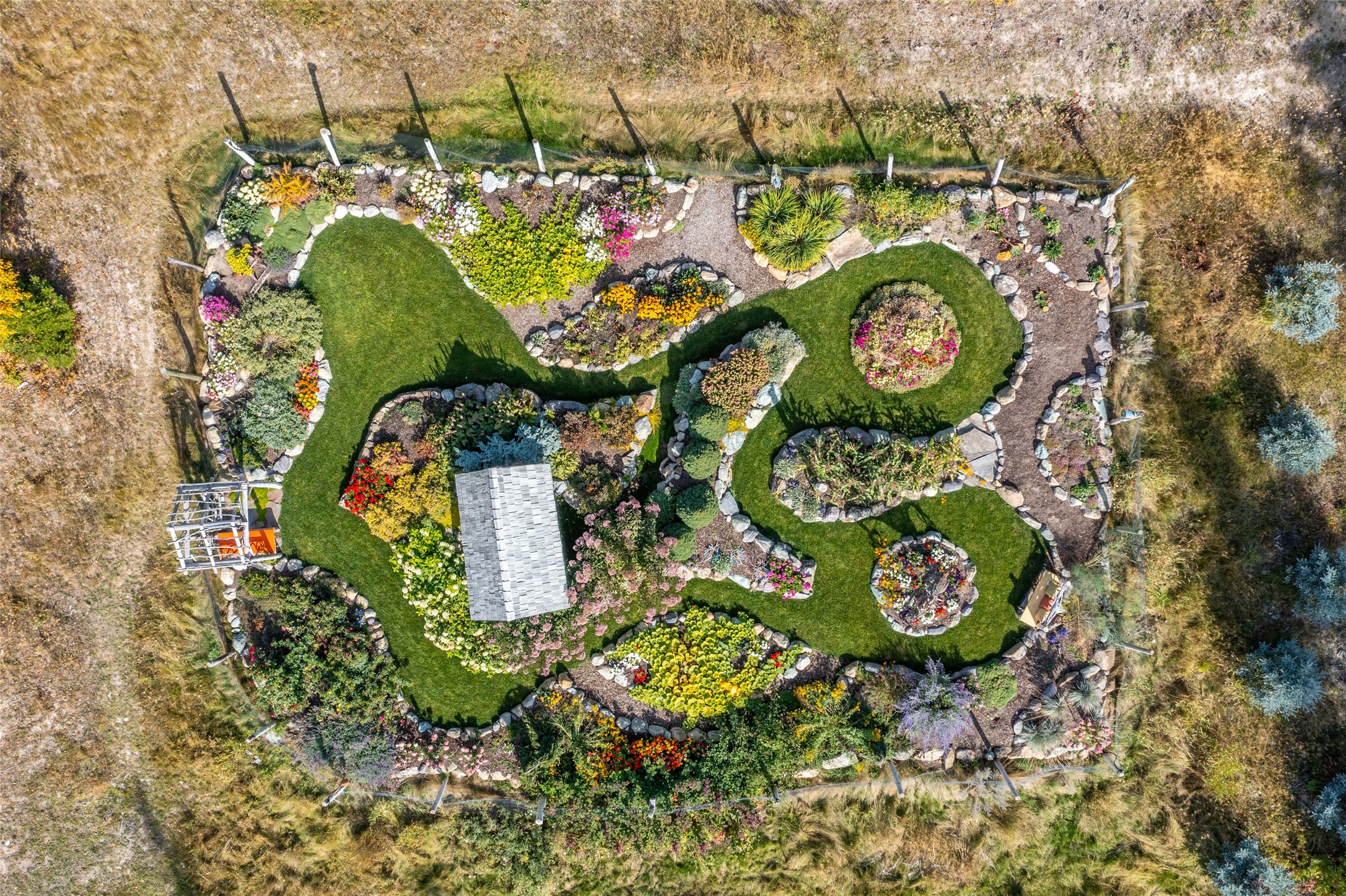 Aerial garden with winding lawns, colorful flower beds, stone borders, and a small pergola.