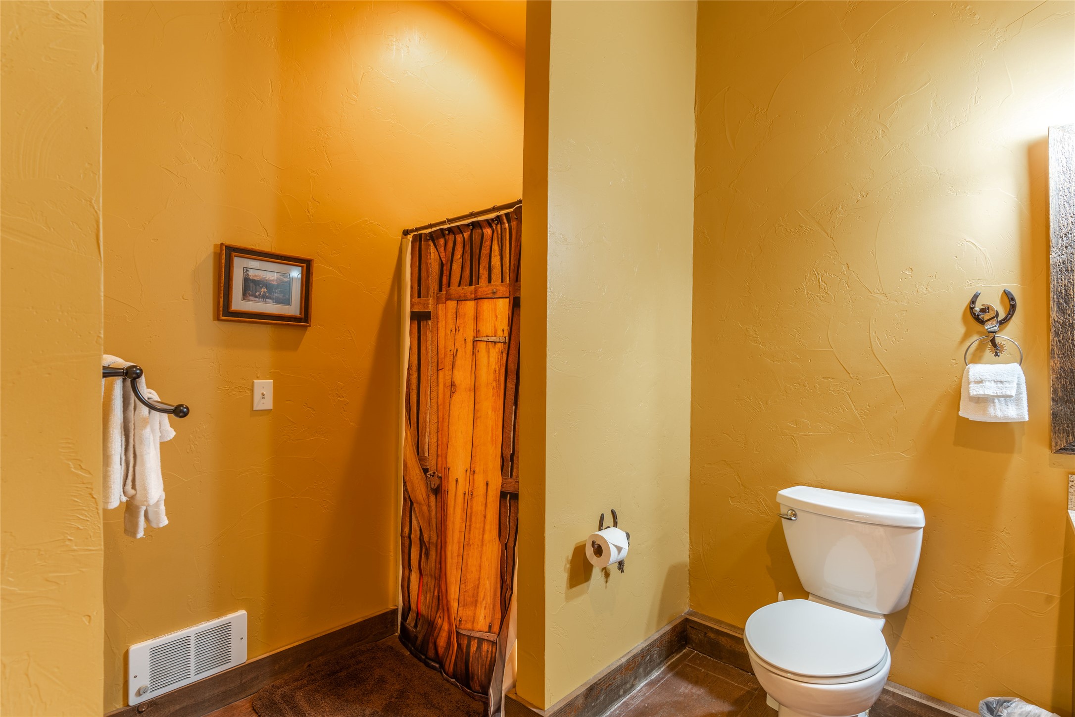 Bathroom with a white toilet and rustic wooden door behind a curtain.