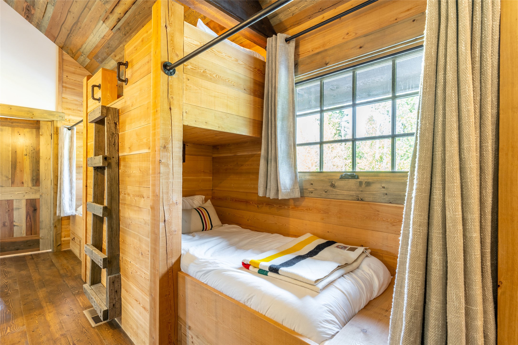 Rustic wood-paneled bedroom with built-in bunks and a large curtained window.