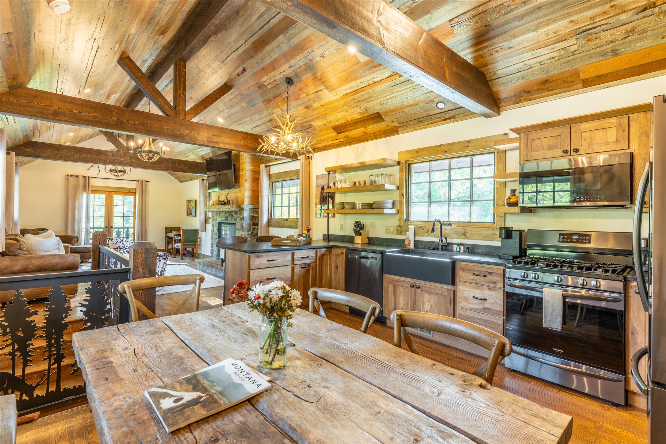 Rustic open-plan kitchen with stainless-steel appliances, a timber dining table, and vaulted exposed-beam ceiling.