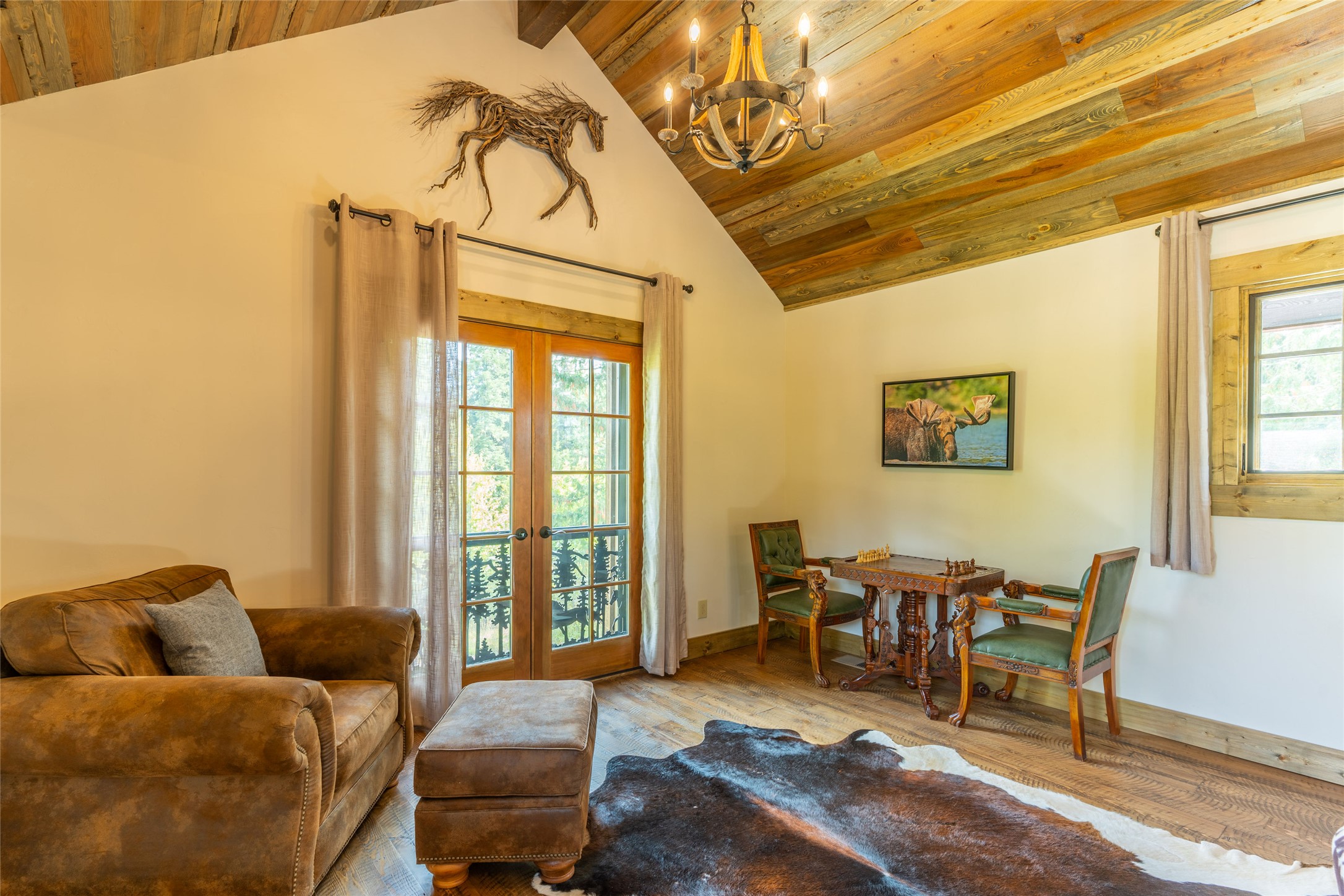 Living room with a vaulted wood ceiling, French doors, leather sofa, and carved chess table.