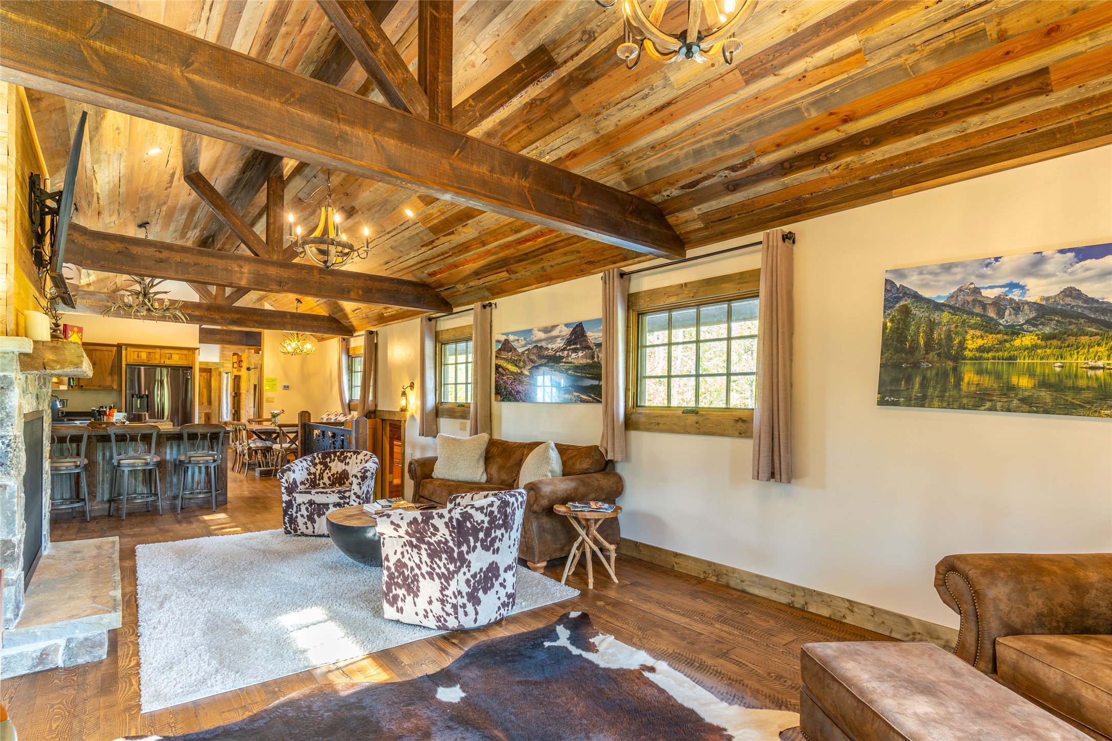 Living room with exposed timber beams, vaulted wood ceiling, stone fireplace, and leather seating.