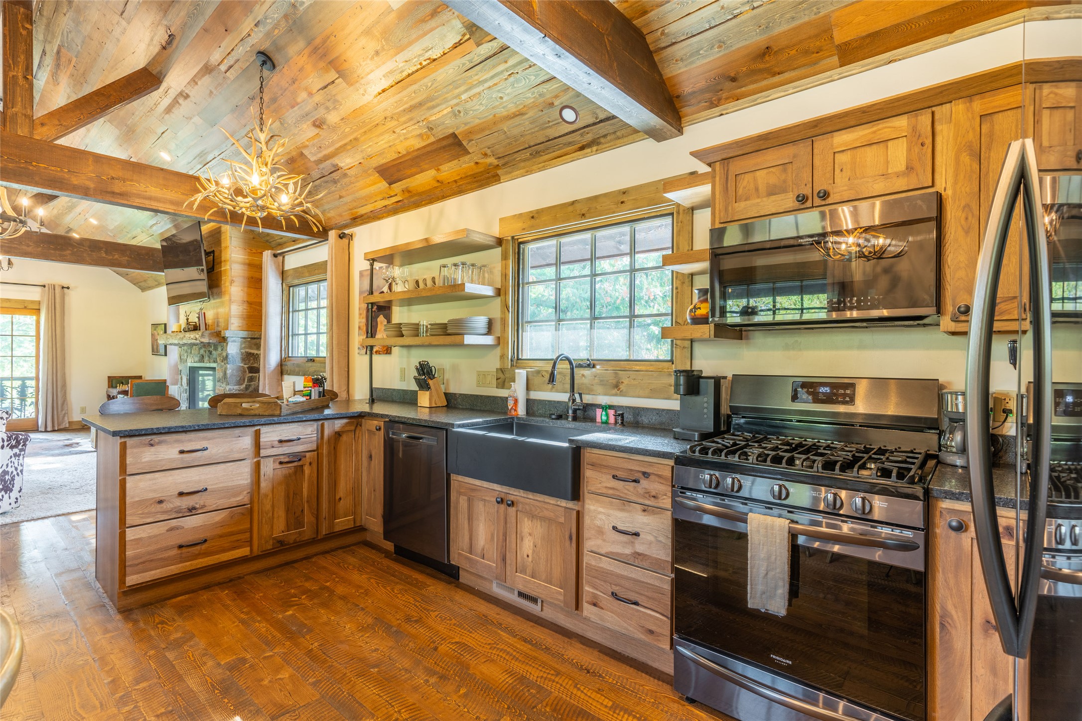 Rustic kitchen with wood cabinets, stainless steel appliances, farmhouse sink, and vaulted timber ceiling.