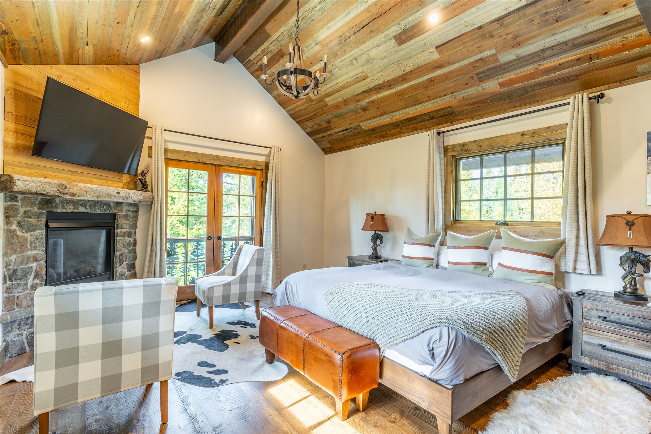 Bedroom with vaulted wood ceiling, stone fireplace, king-size bed, and French doors.