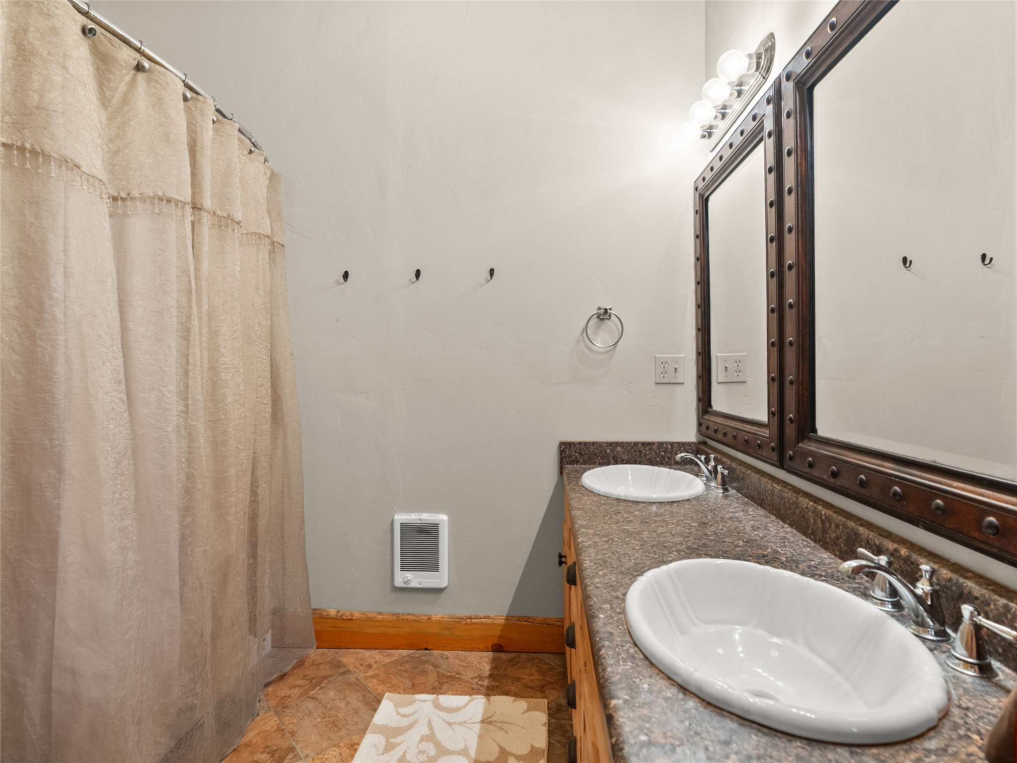 Bathroom with a double-sink vanity, dark stone counter, and large framed mirror.