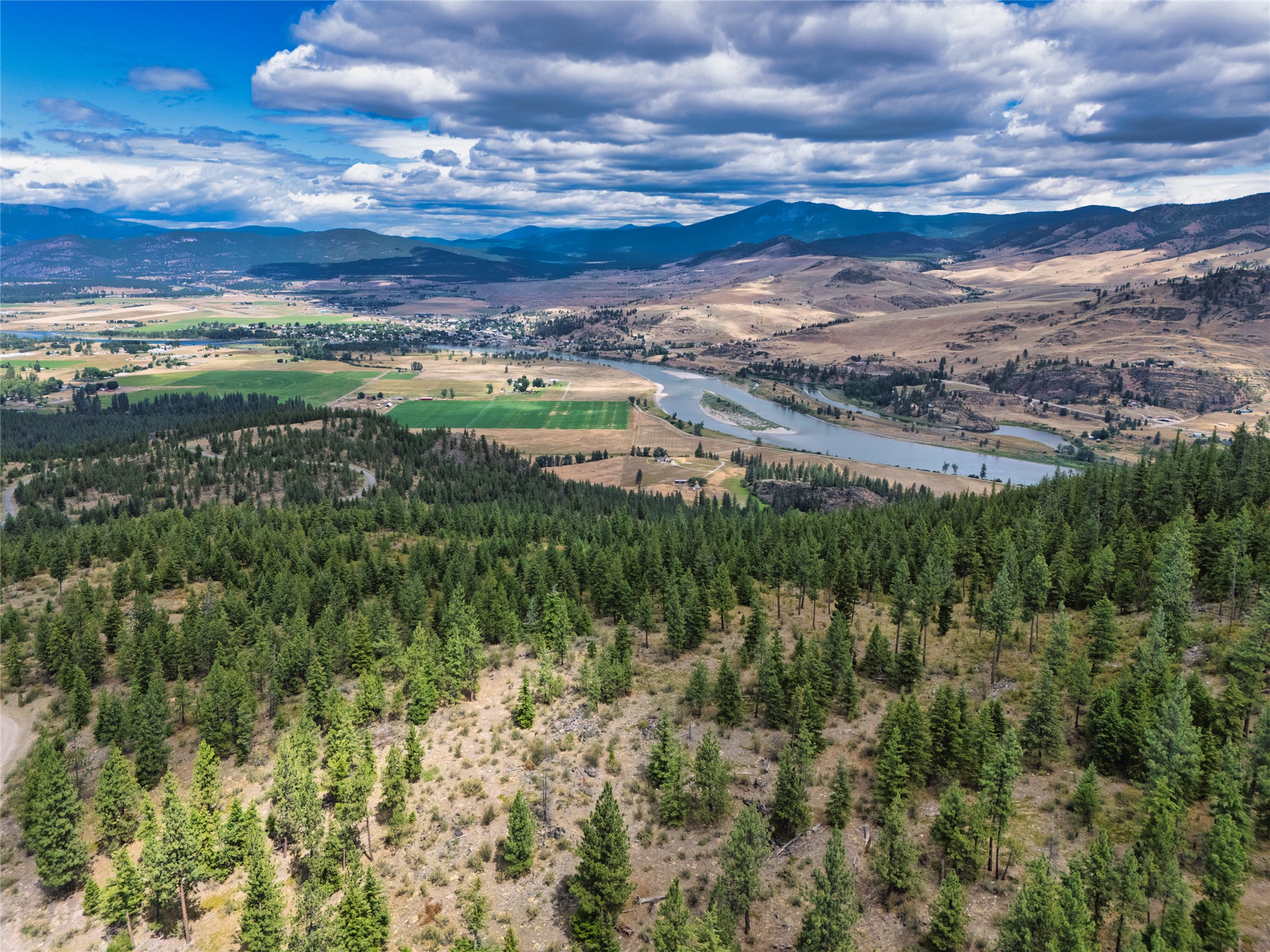 Aerial view across a wooded property toward a winding river, valley farmland, and distant mountains.