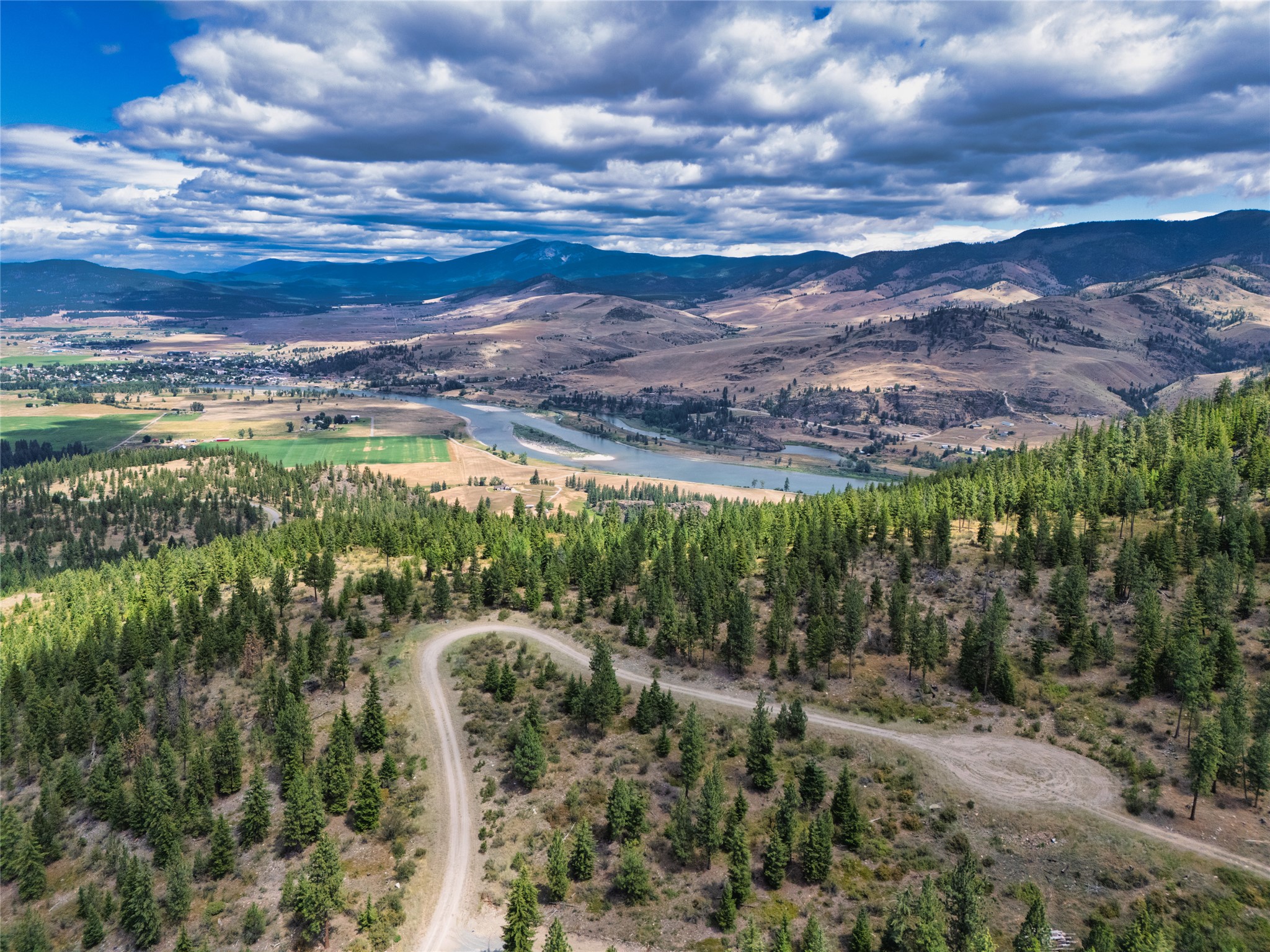Aerial view of wooded land and a dirt road overlooking a river valley and mountains.