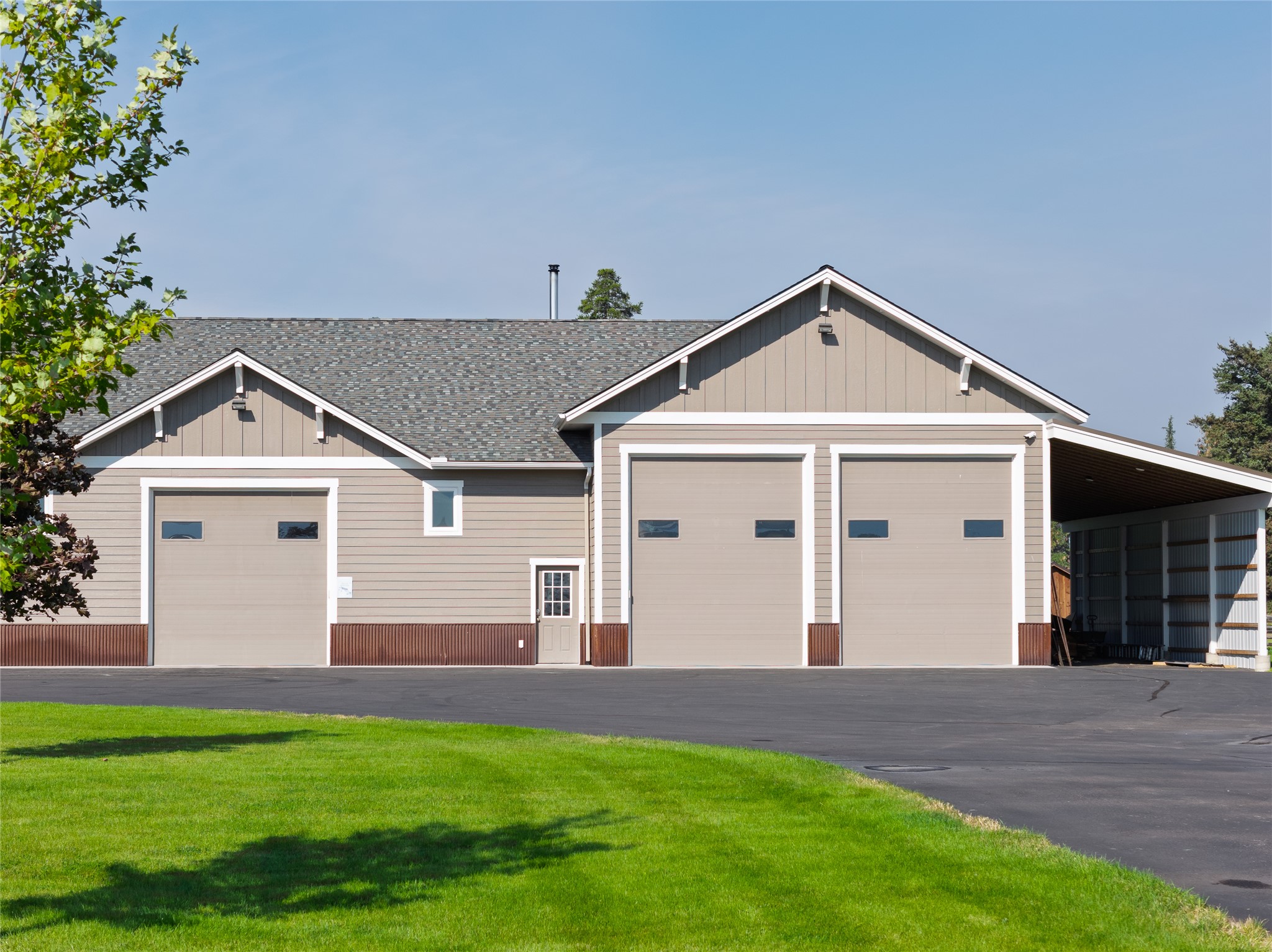 Beige workshop with three garage doors and an open-sided covered bay beside a paved driveway.