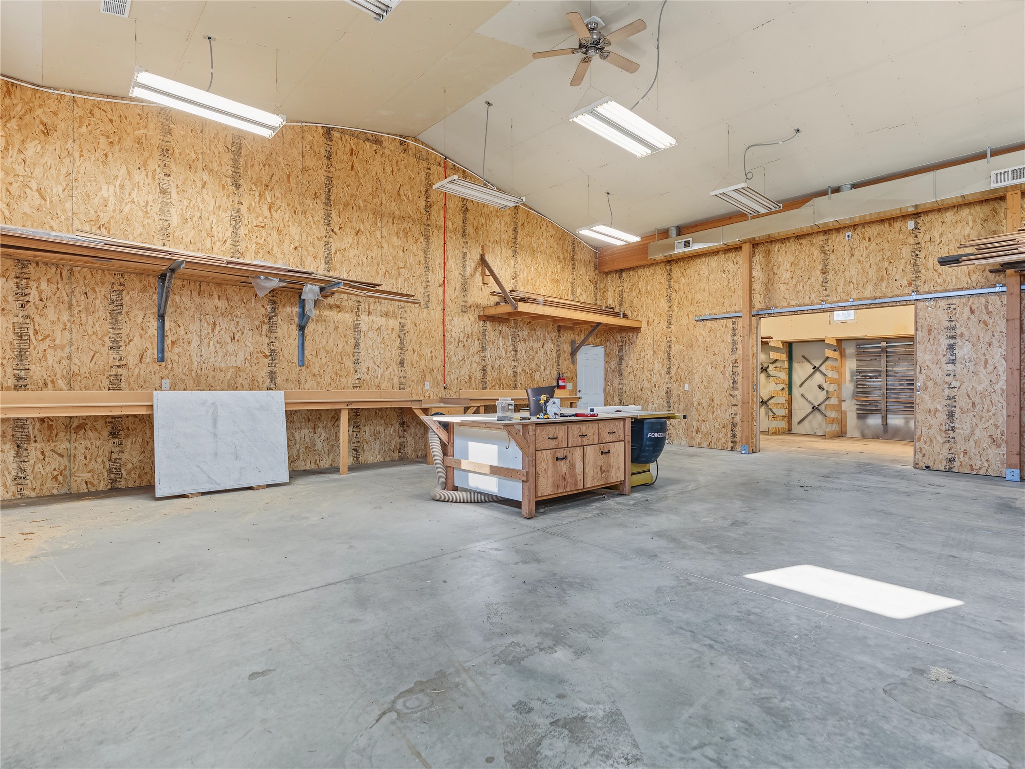 Woodworking workshop with wall-mounted lumber racks and a central workbench.