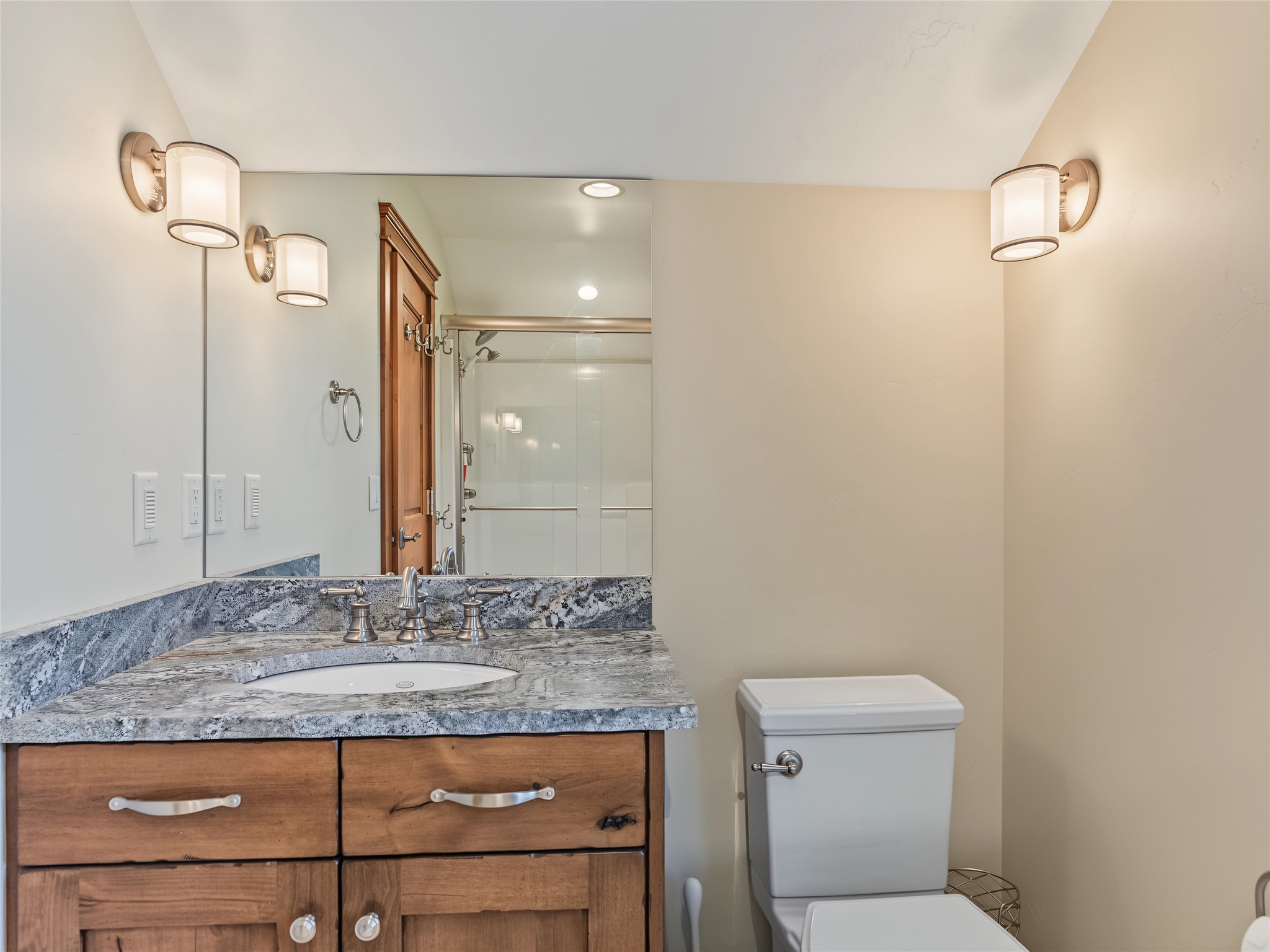 Bathroom with a granite vanity, wood cabinetry, large mirror, and glass-enclosed shower.