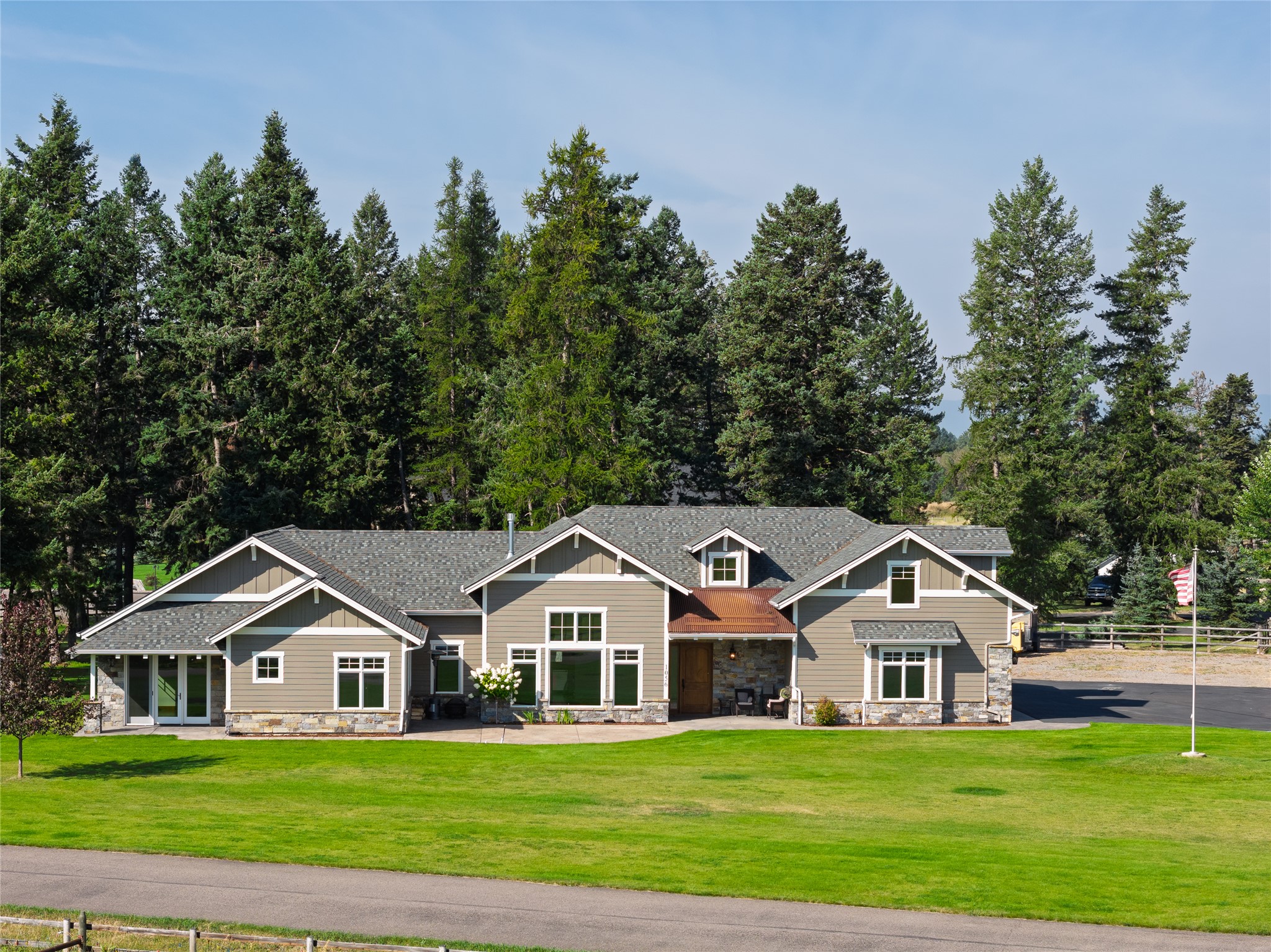 Gray gabled home with stone accents, a broad green lawn, and tall evergreens behind it.