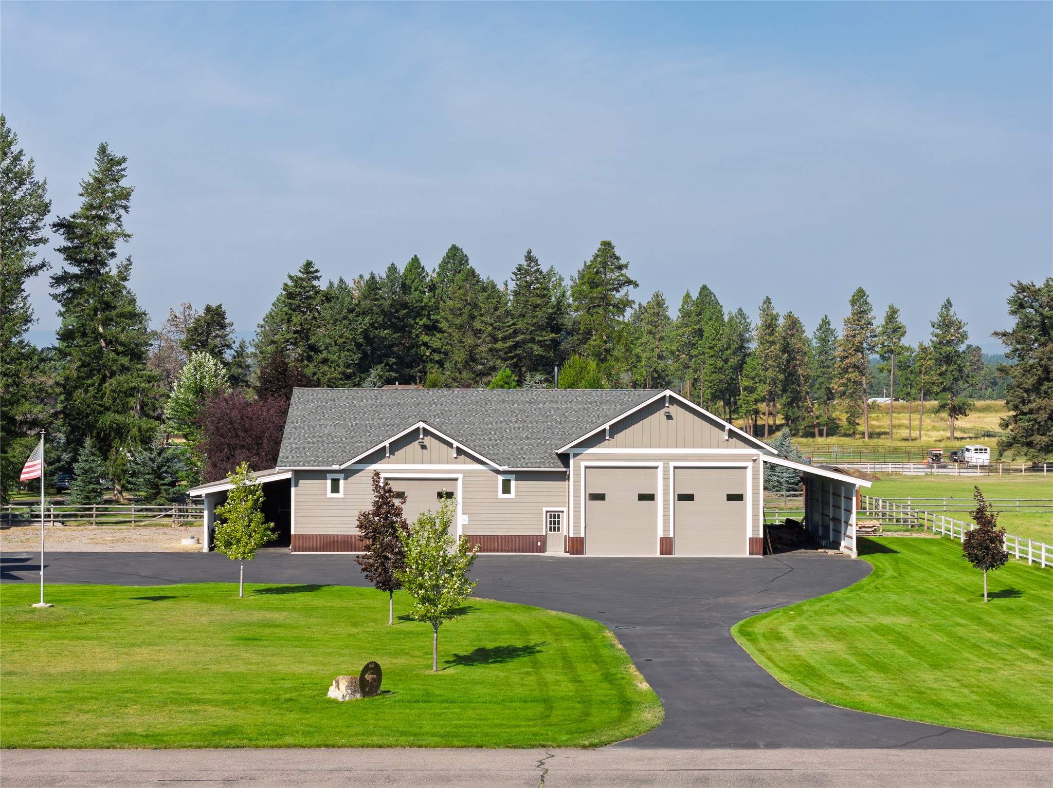 Large taupe outbuilding with two garage doors and a covered side area beside a curved driveway and lawn.