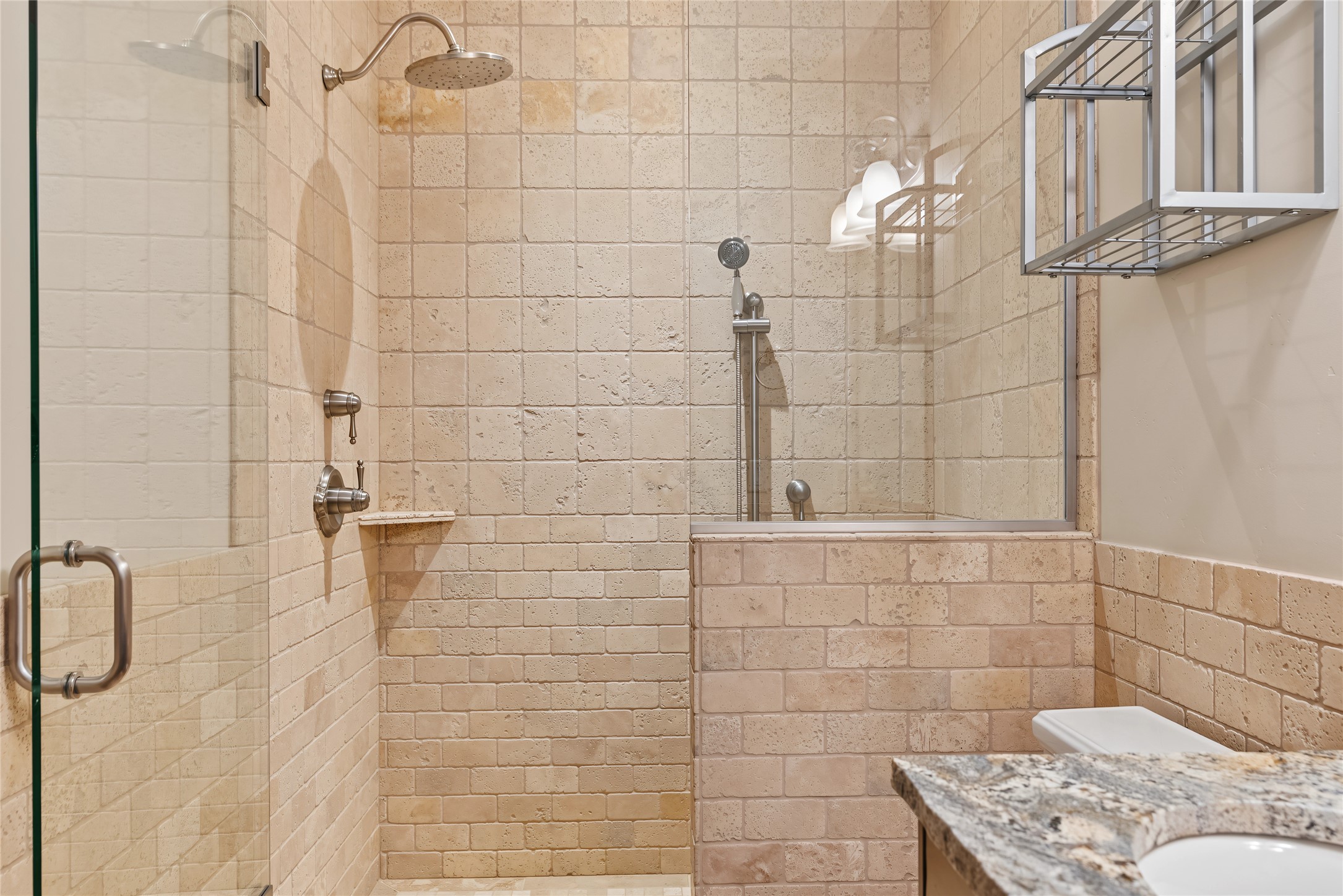 Bathroom shower with beige stone tile, rainfall showerhead, and granite vanity.