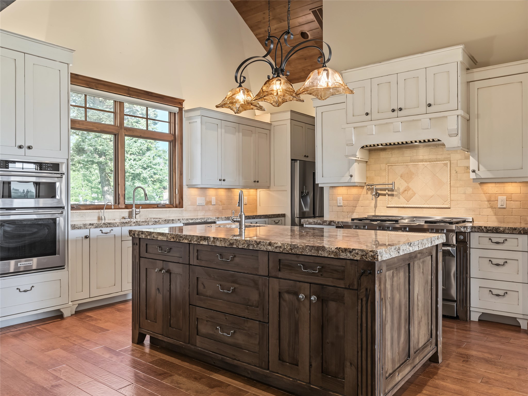 Kitchen with a large dark wood island, white cabinetry, stainless steel appliances, and three pendant lights.