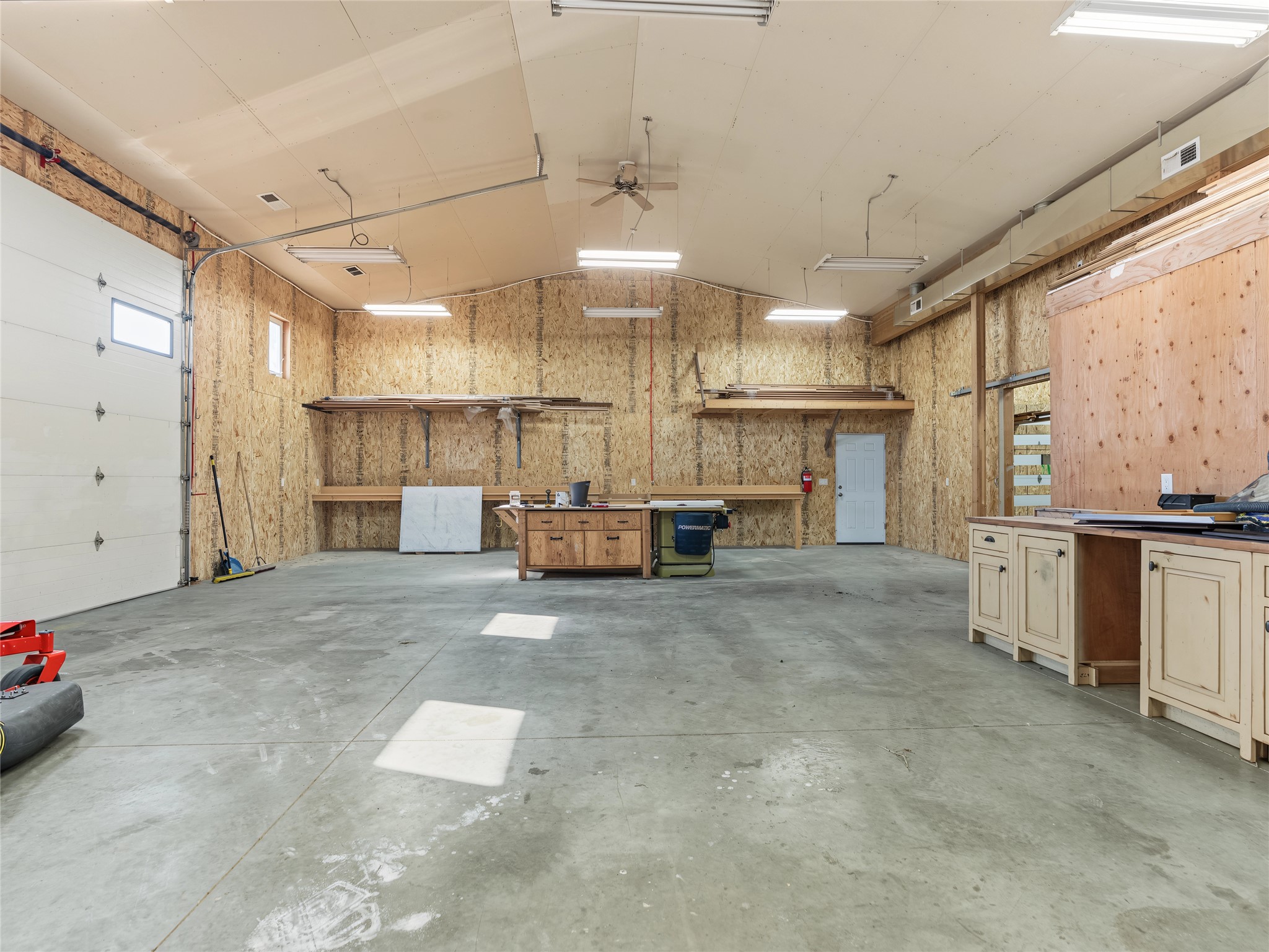 Spacious workshop garage with a large overhead door, concrete floor, and built-in workbenches.