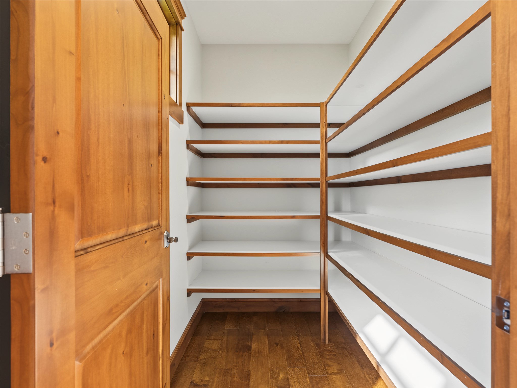 Empty walk-in pantry with wood-trimmed shelves and dark hardwood flooring.