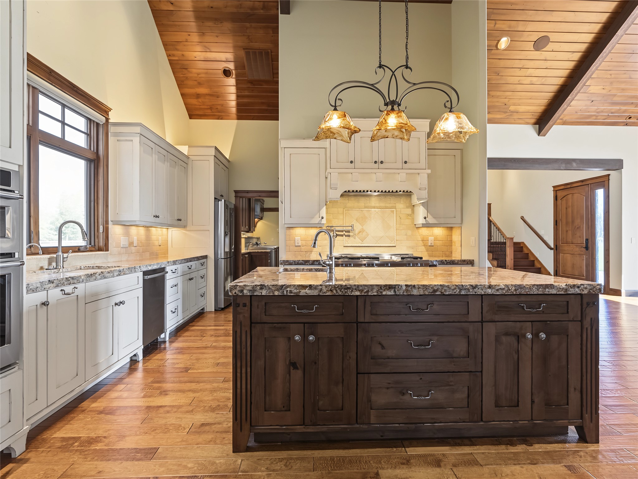 Kitchen with a large dark-wood island, white cabinetry, stone counters, and vaulted wood ceilings.