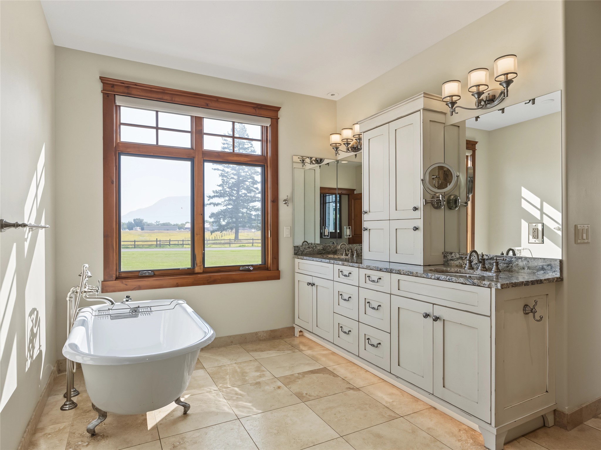 Bathroom with a freestanding tub, long white vanity, and a large wood-trimmed window overlooking a field.