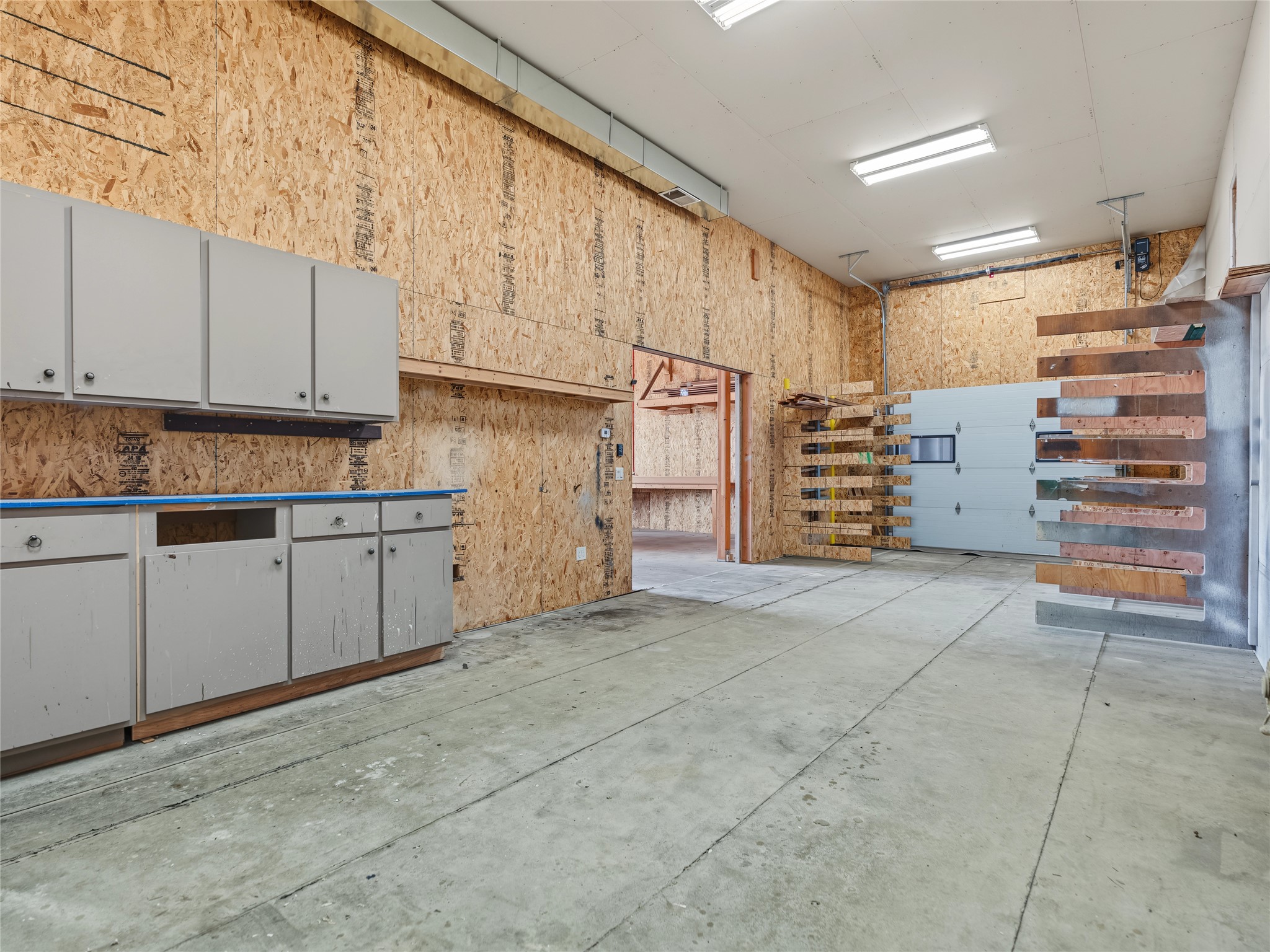 Garage workshop with built-in cabinets, lumber racks, exposed wood walls, and a concrete floor.