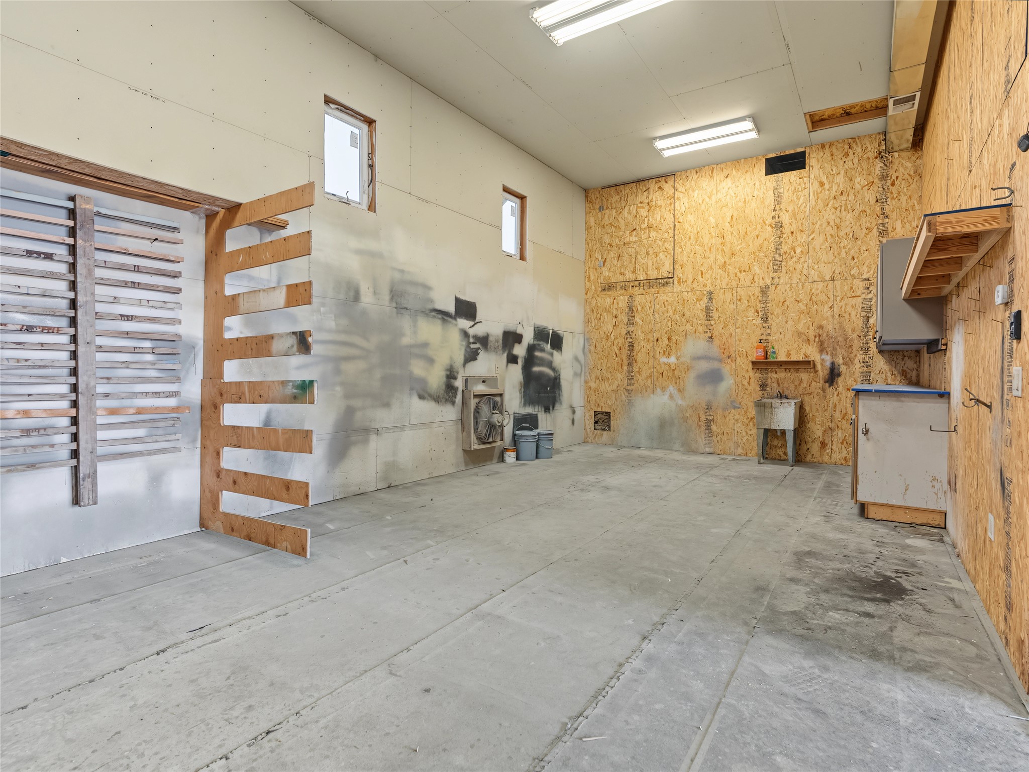 Unfinished garage with a broad concrete floor, exposed OSB walls, and built-in shelving.