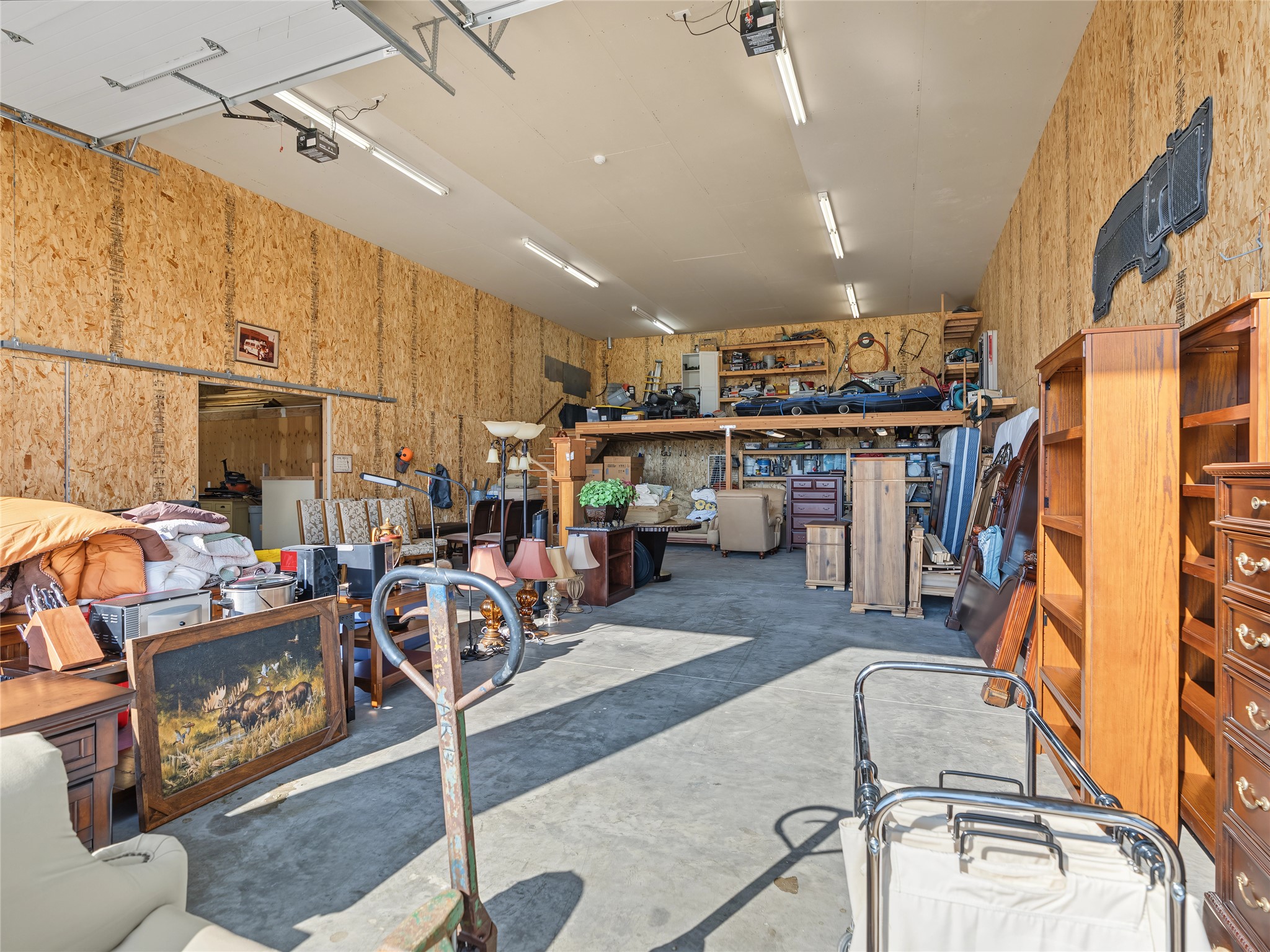 Garage crowded with stored furniture and household items, with boats and gear on a raised rack.