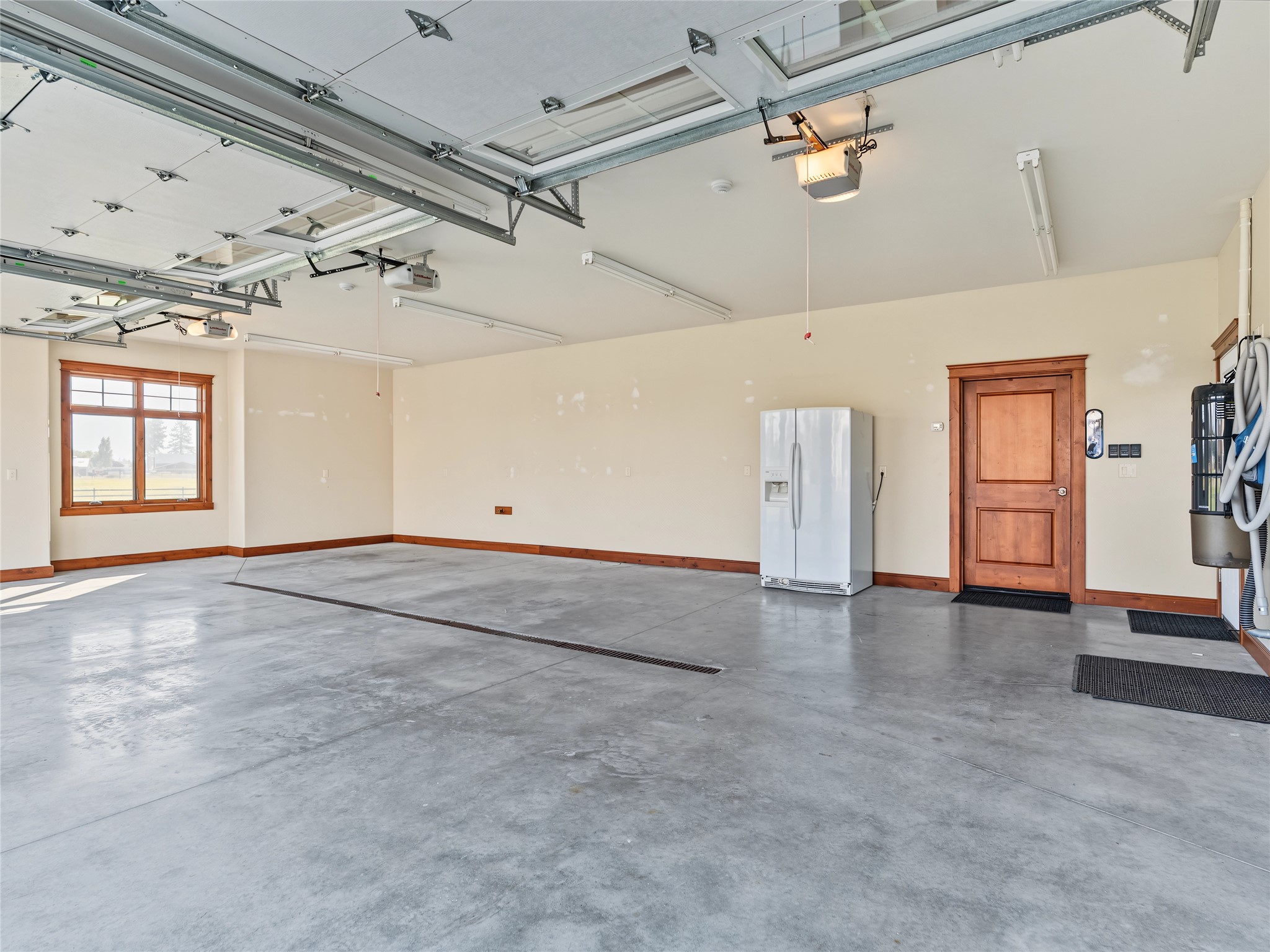 Spacious empty garage with concrete floors, multiple overhead doors, and a refrigerator.