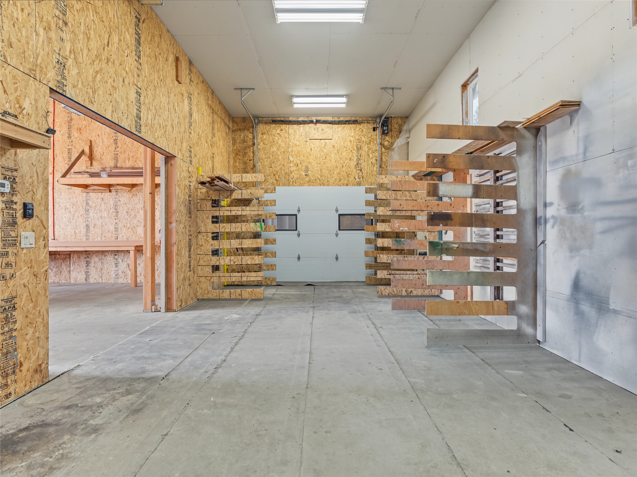 Unfinished garage with exposed OSB walls, concrete floor, and heavy-duty wooden storage racks.