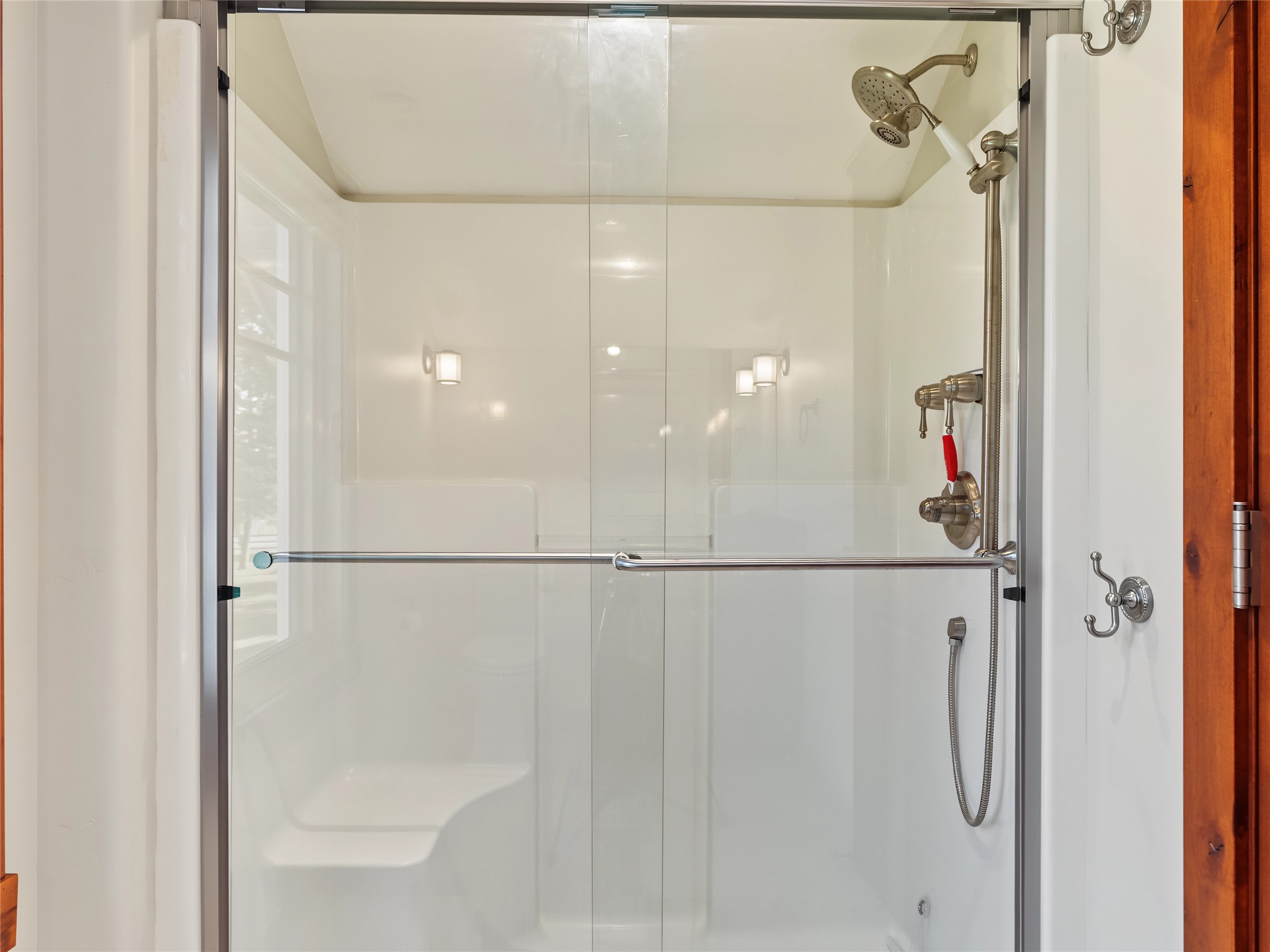 Walk-in shower with clear glass doors, chrome fixtures, a grab bar, and a built-in seat.