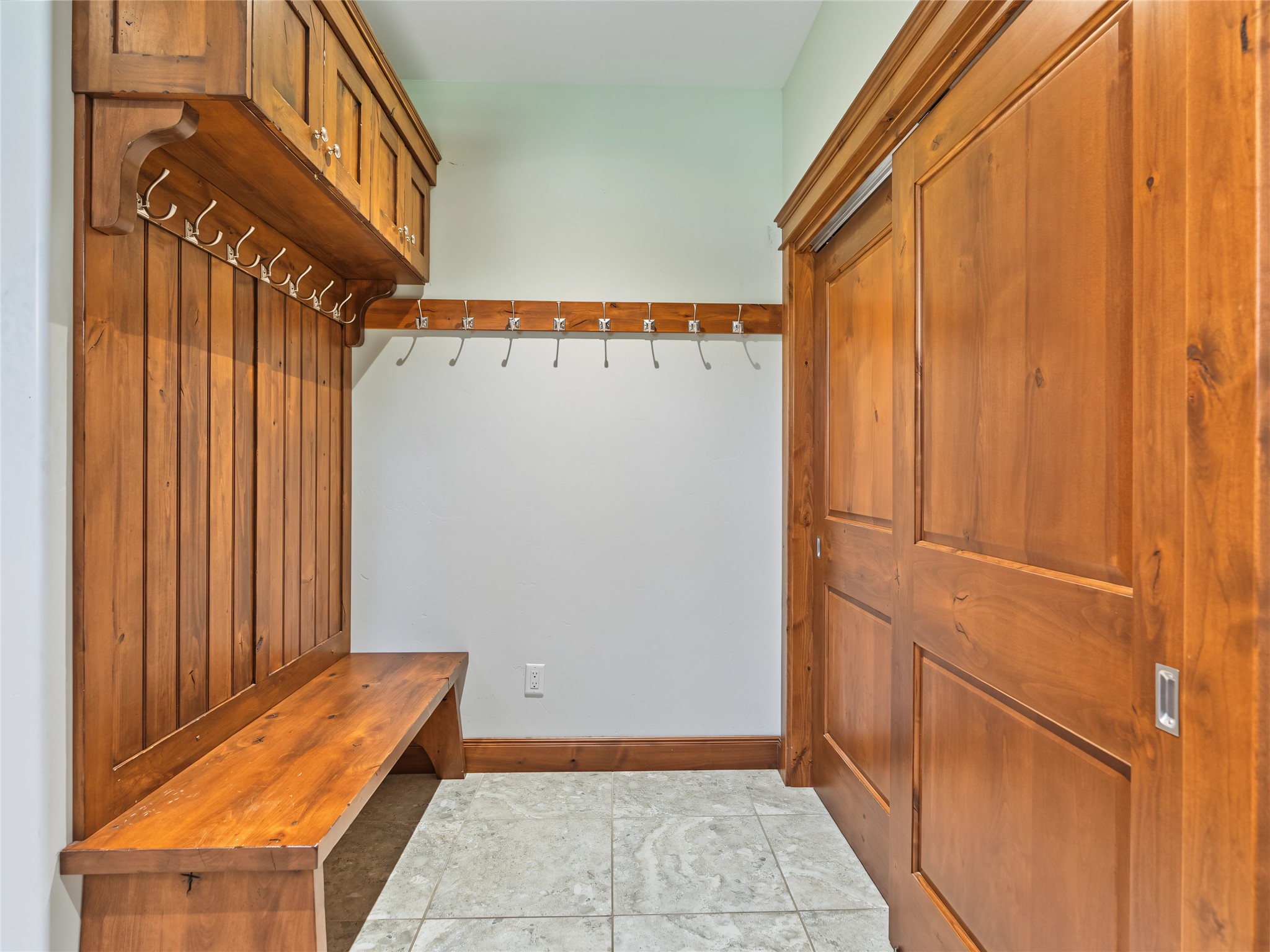 Mudroom with wood built-in bench and hooks, tiled floor, and sliding barn doors.