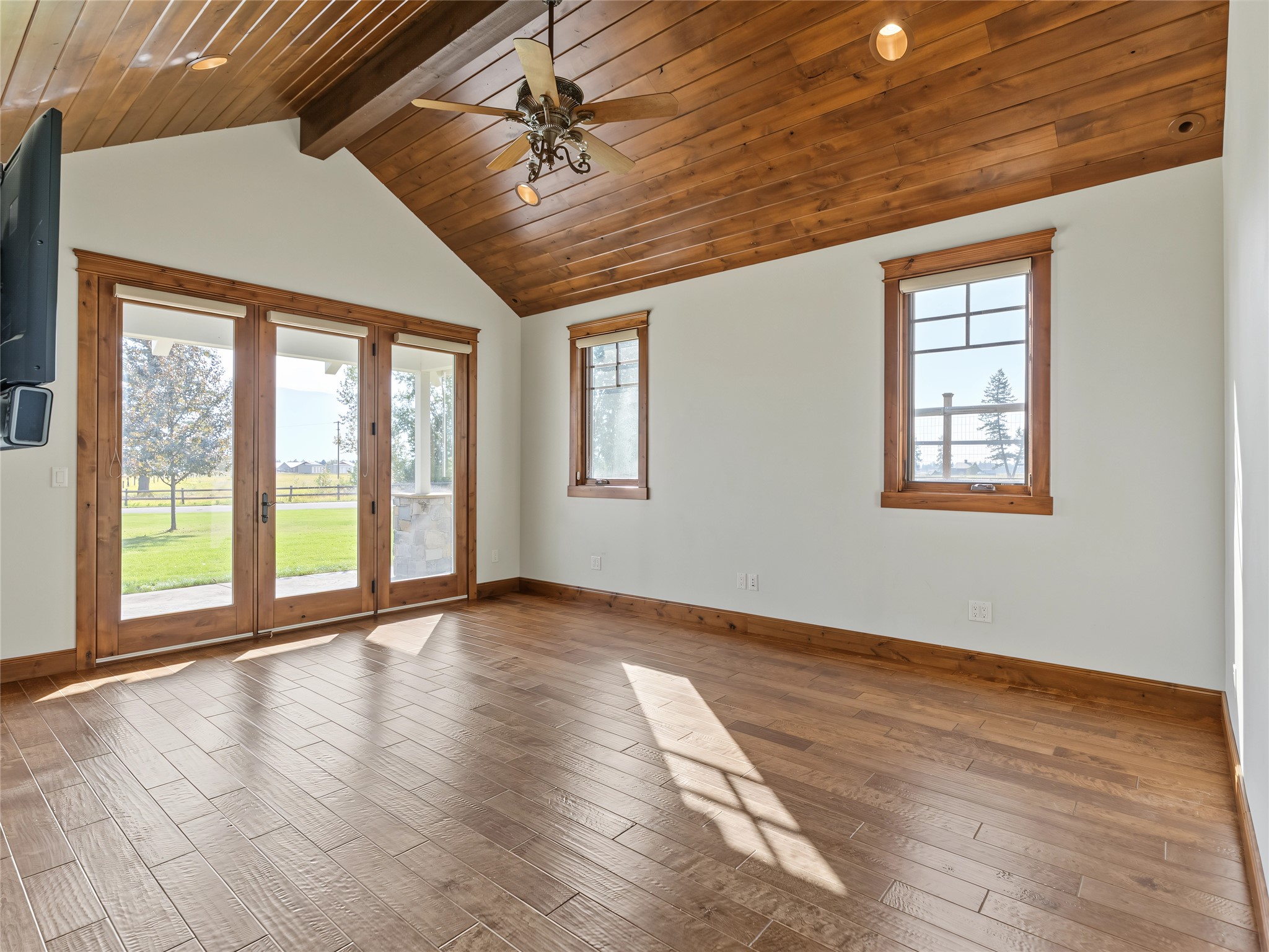 Empty room with a vaulted wood ceiling, wood-look floors, and glass doors opening to a lawn.