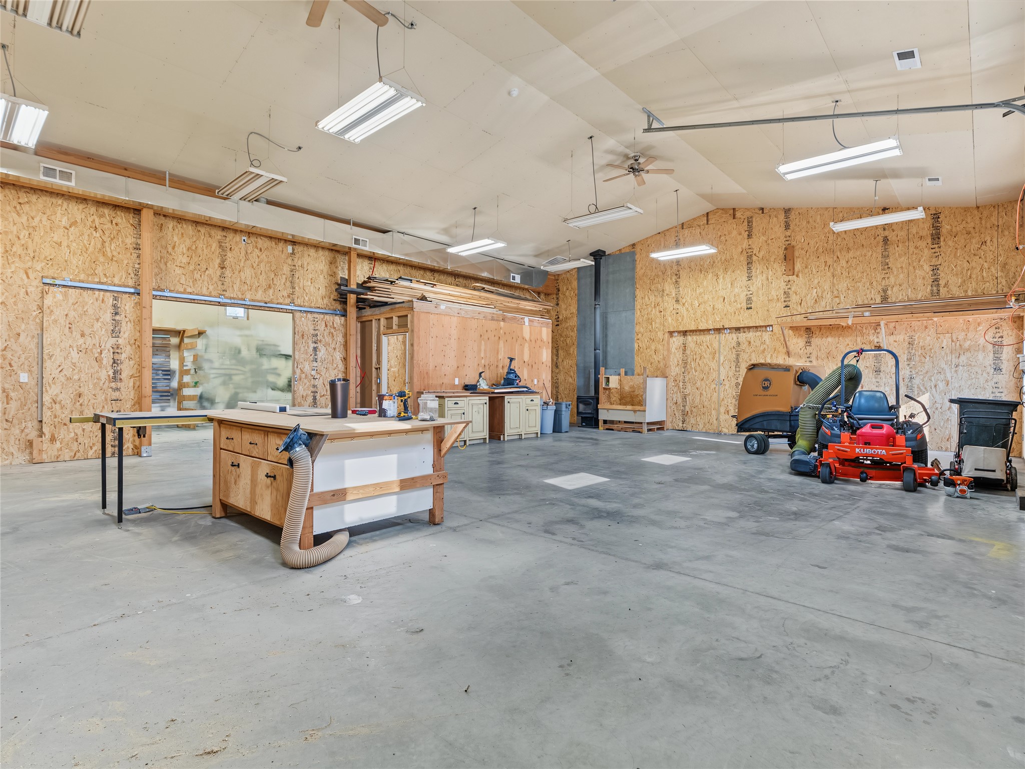 Spacious workshop with plywood walls, workbenches, woodworking equipment, and a red riding mower.