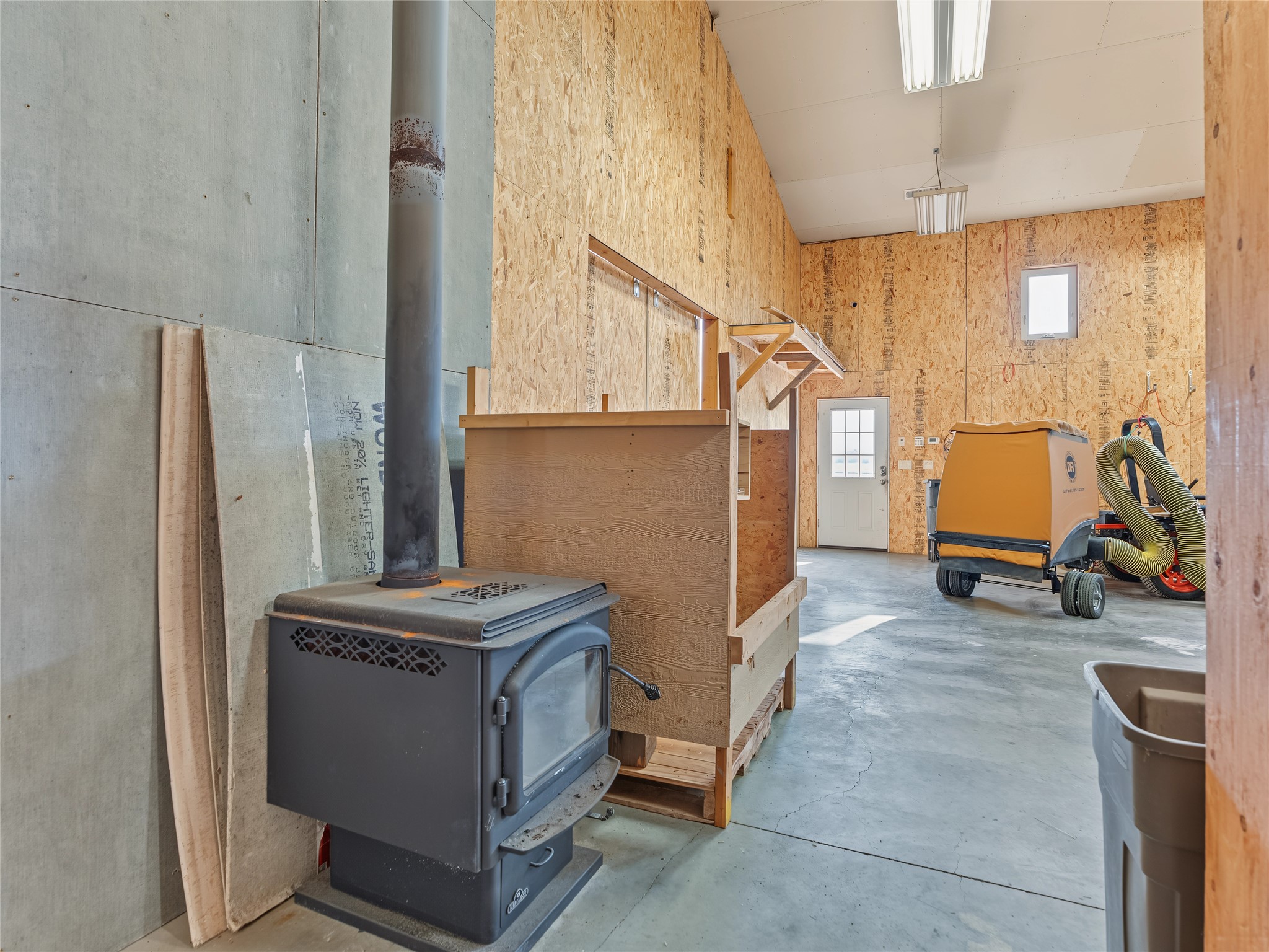 Workshop with exposed OSB walls, concrete floor, wood stove, and dust-collection machine.