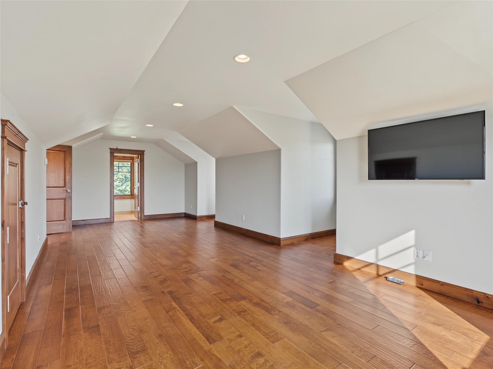 Vacant room with vaulted ceiling, wood plank floors, and a wall-mounted television.