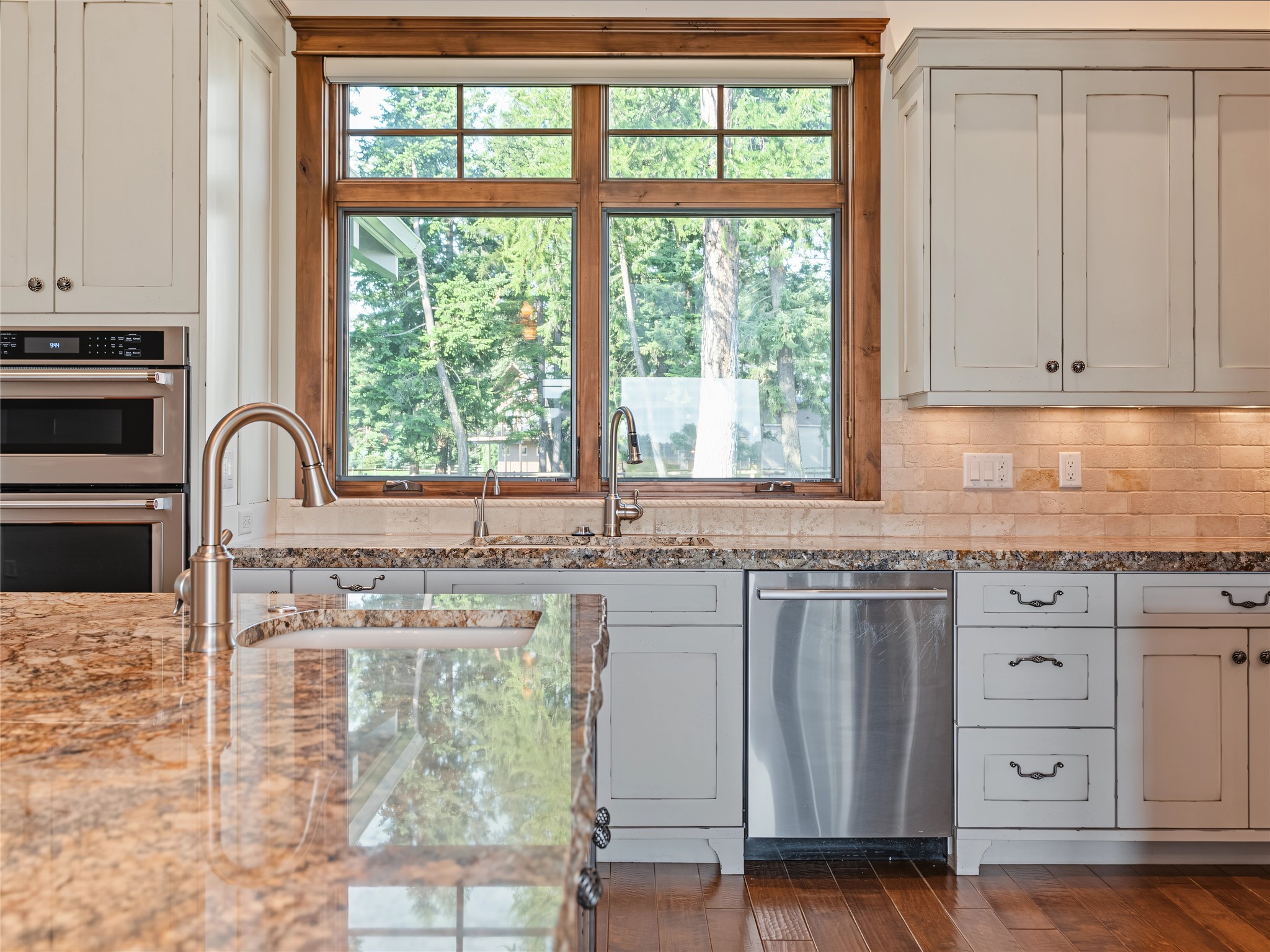 Kitchen with granite counters, white cabinetry, stainless steel appliances, and a large wood-trimmed window.